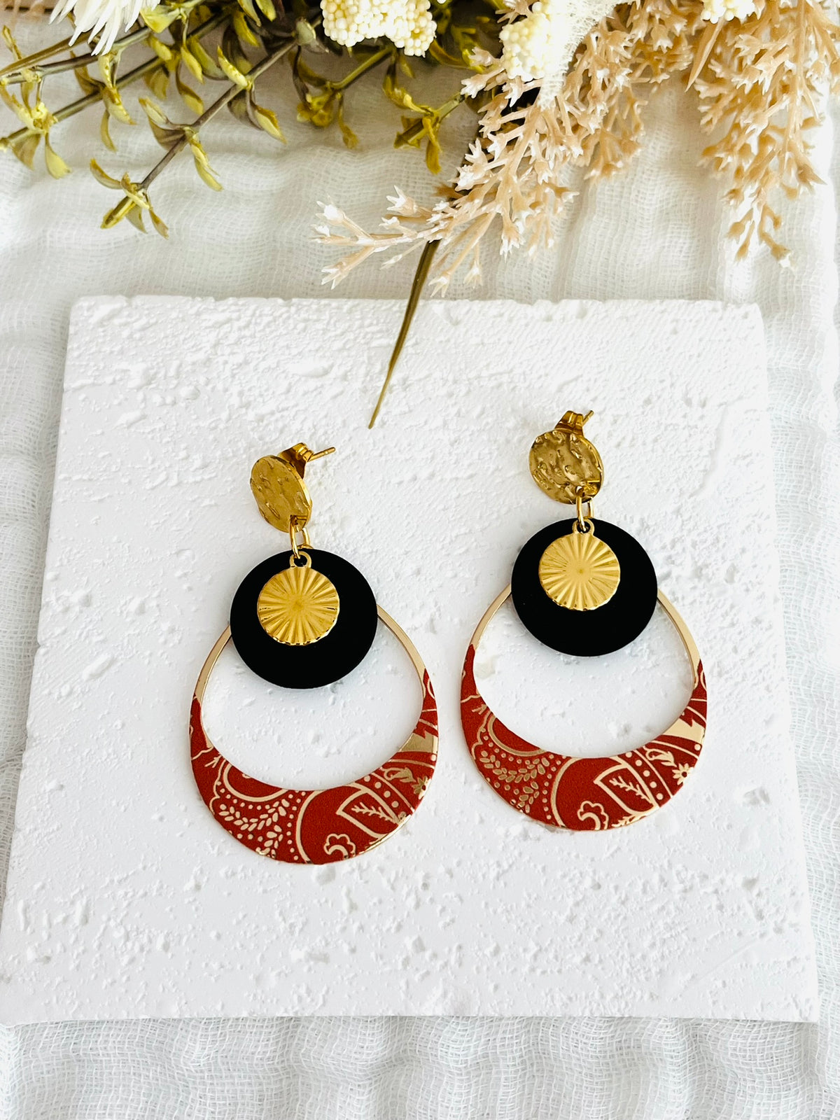 Boucles d'oreilles fantaisie fait main.
Clous d'oreilles ronds martelés en acier doré. Sequins ronds noir mat, pendentif goutte motif bandana terracotta et doré.
Bijou fantaisie fait main.