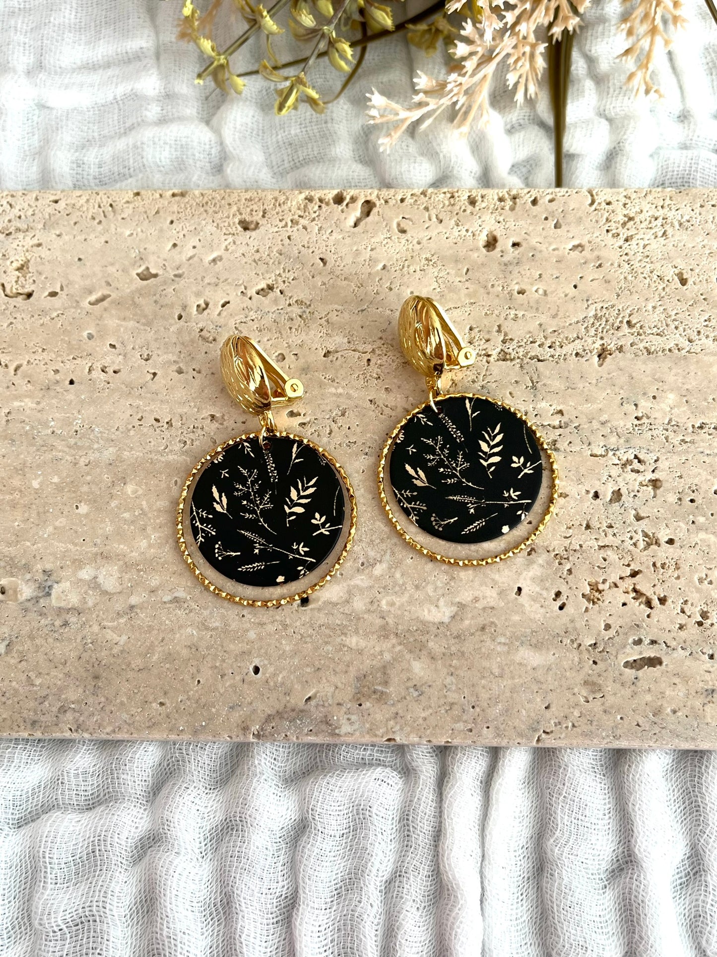 Boucles d'oreilles à clip fantaisie fait main.
Clip doré à l'or fin. Anneaux ciselés en acier inoxydable doré. Pendentifs ronds noir imprimé feuilles doré.
Bijou fantaisie fait main
