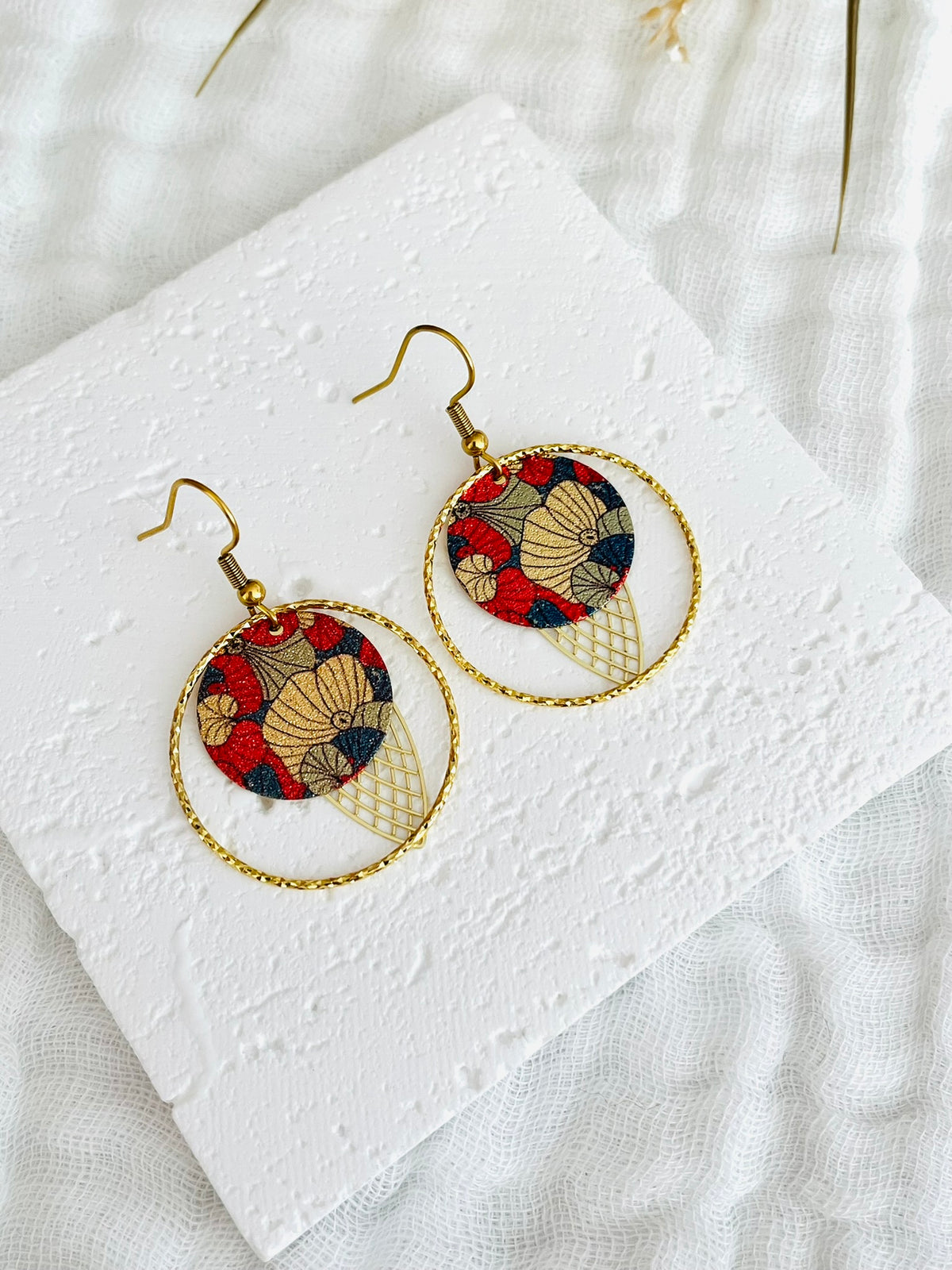 Boucles d'oreilles fantaisie fait main.
Crochets d'oreilles en acier inox doré; anneaux fermés ciseles en laiton or 18; estampe navette filigranée doré, sequin rond pailleté motif fleur bleu et rouge.
Bijou fait main.