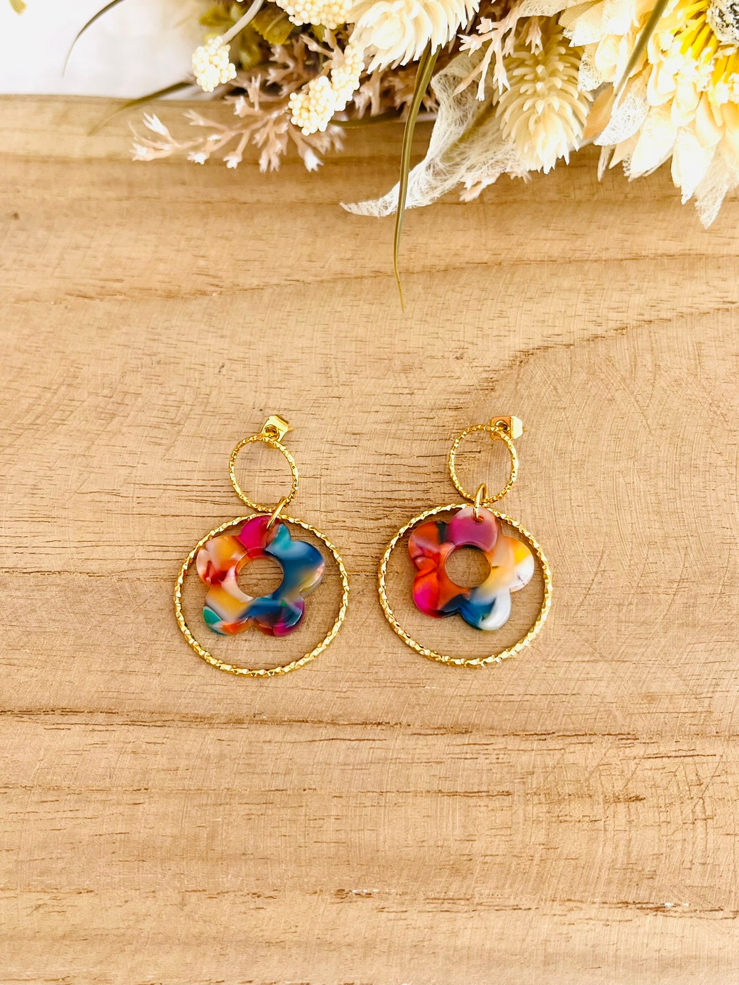 Boucles d'oreilles fantaisie fait main.
Clous d'oreilles ronds en acier inox doré, anneau fermé ciselé en acier doré, fleur multicolore en acrylique.
Bijou fantaisie fait main.