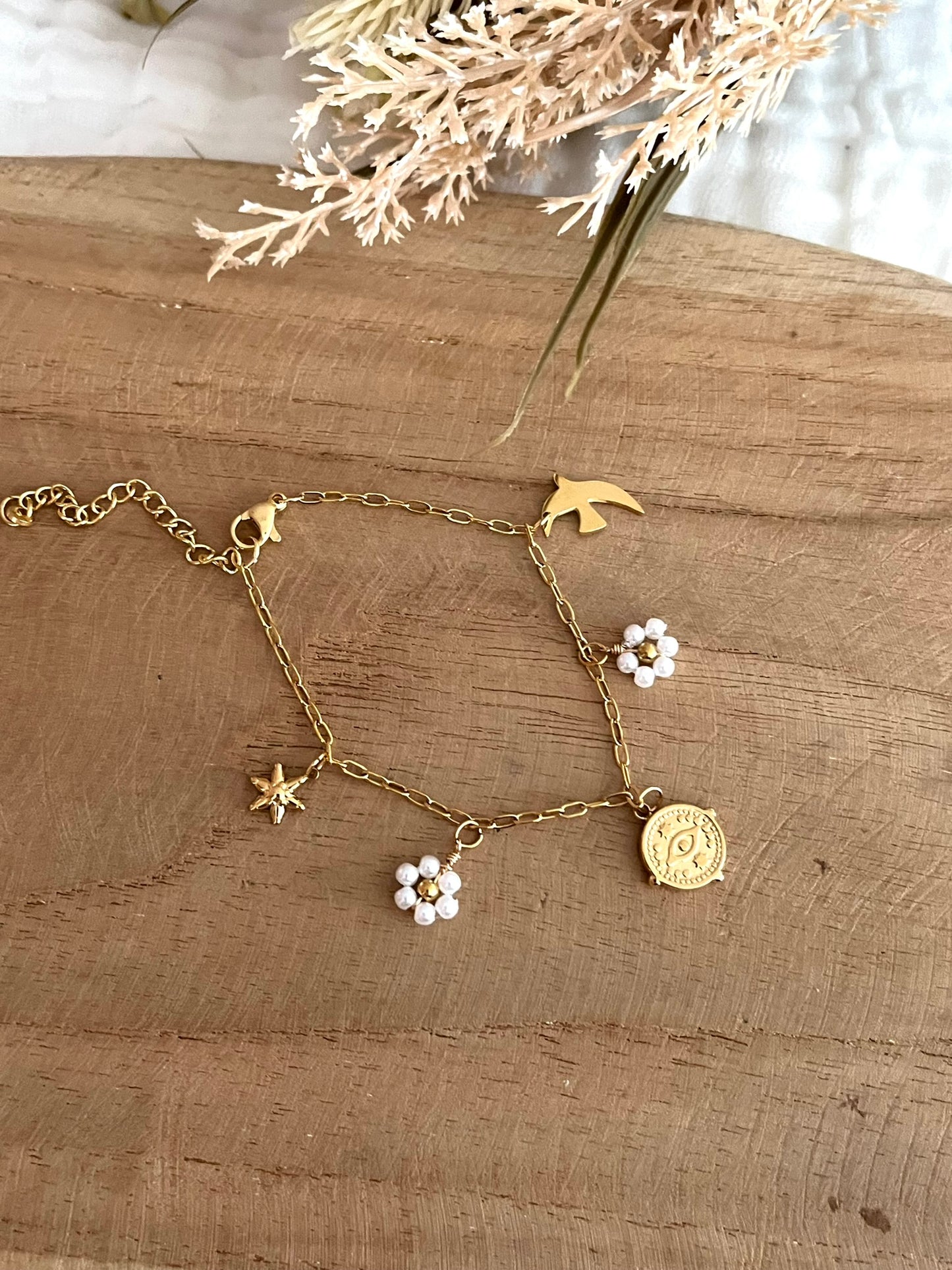 Bracelet fantaisie fait main.
Bracelet à charms en acier inoxydable doré orné de fleurs perlées blanc nacré, une hirondelle, une étoile et une breloque oeil protecteur en acier doré.
Bijou fantaisie fait main.