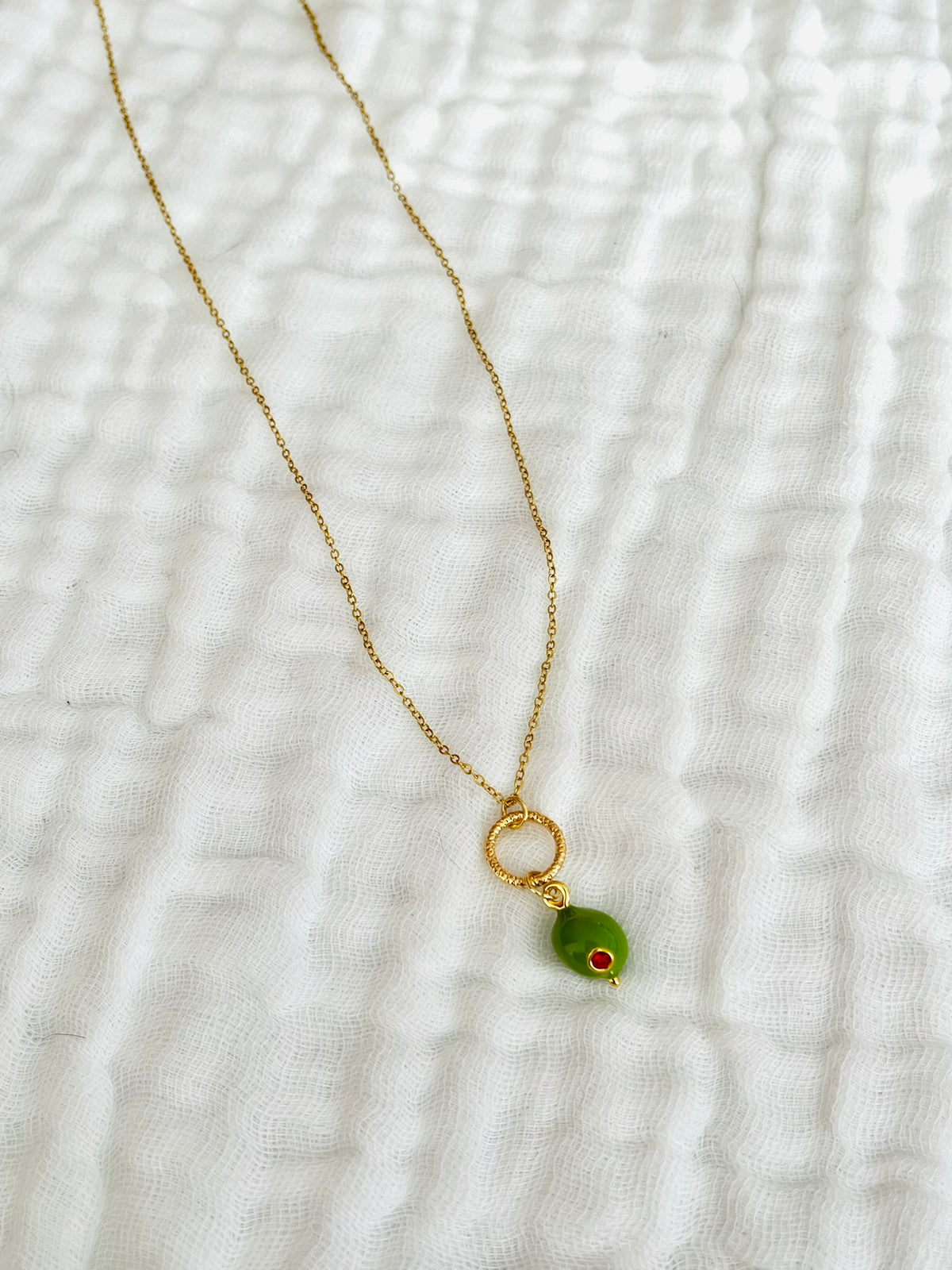Collier fantaisie fait main
Chaîne en acier inox doré, anneau ciselé en laiton doré à l'or fin. Pendentif boule en laiton vert olive avec un strass rouge.
Bijou fantaisie fait main.