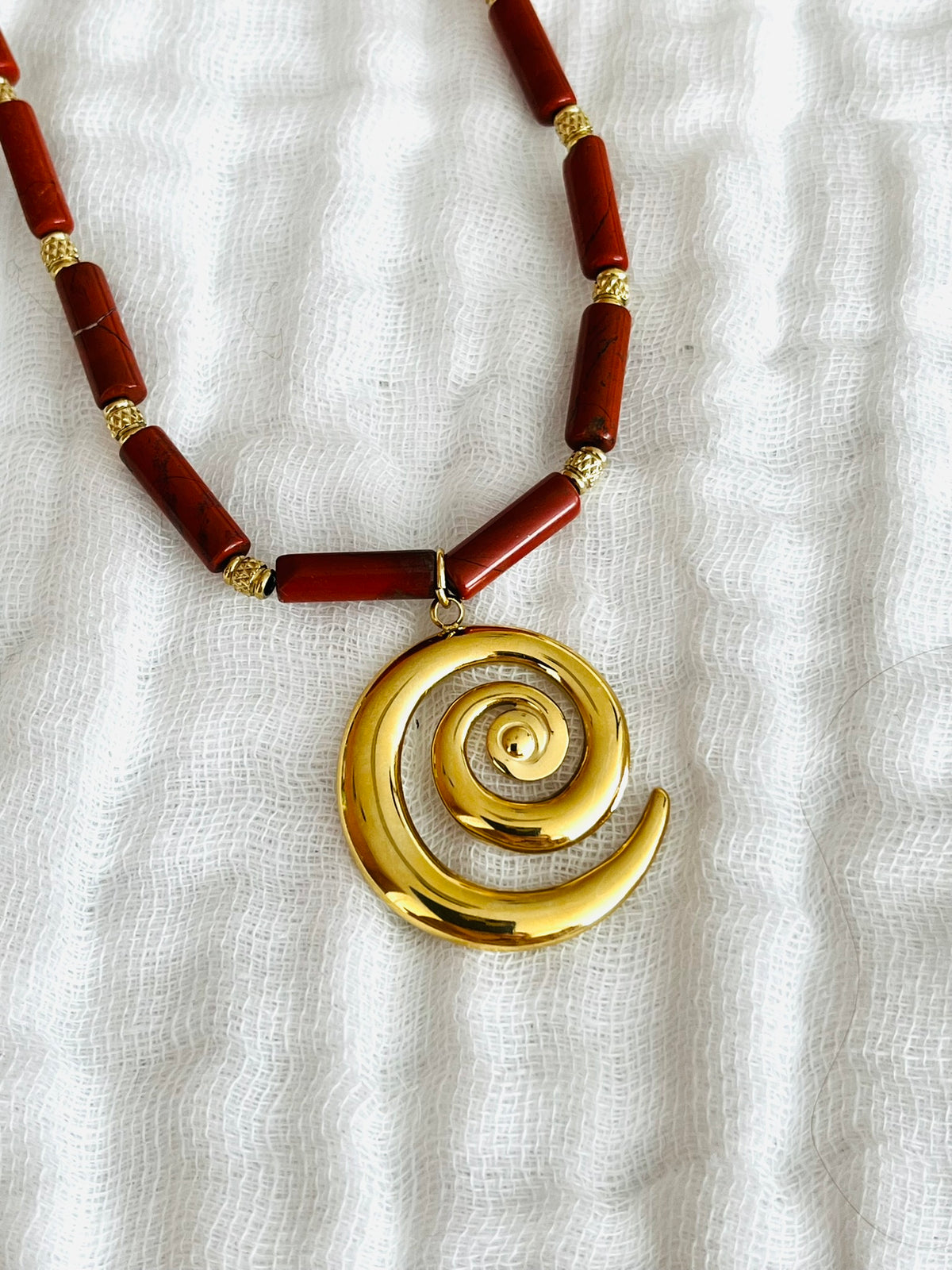 Collier fantaisie fait main.
Chaîne en acier doré et perles tubes en pierre naturelle jaspe rouge rouille.
Pendentif spirale en acier inox doré.
Bijou fait main.