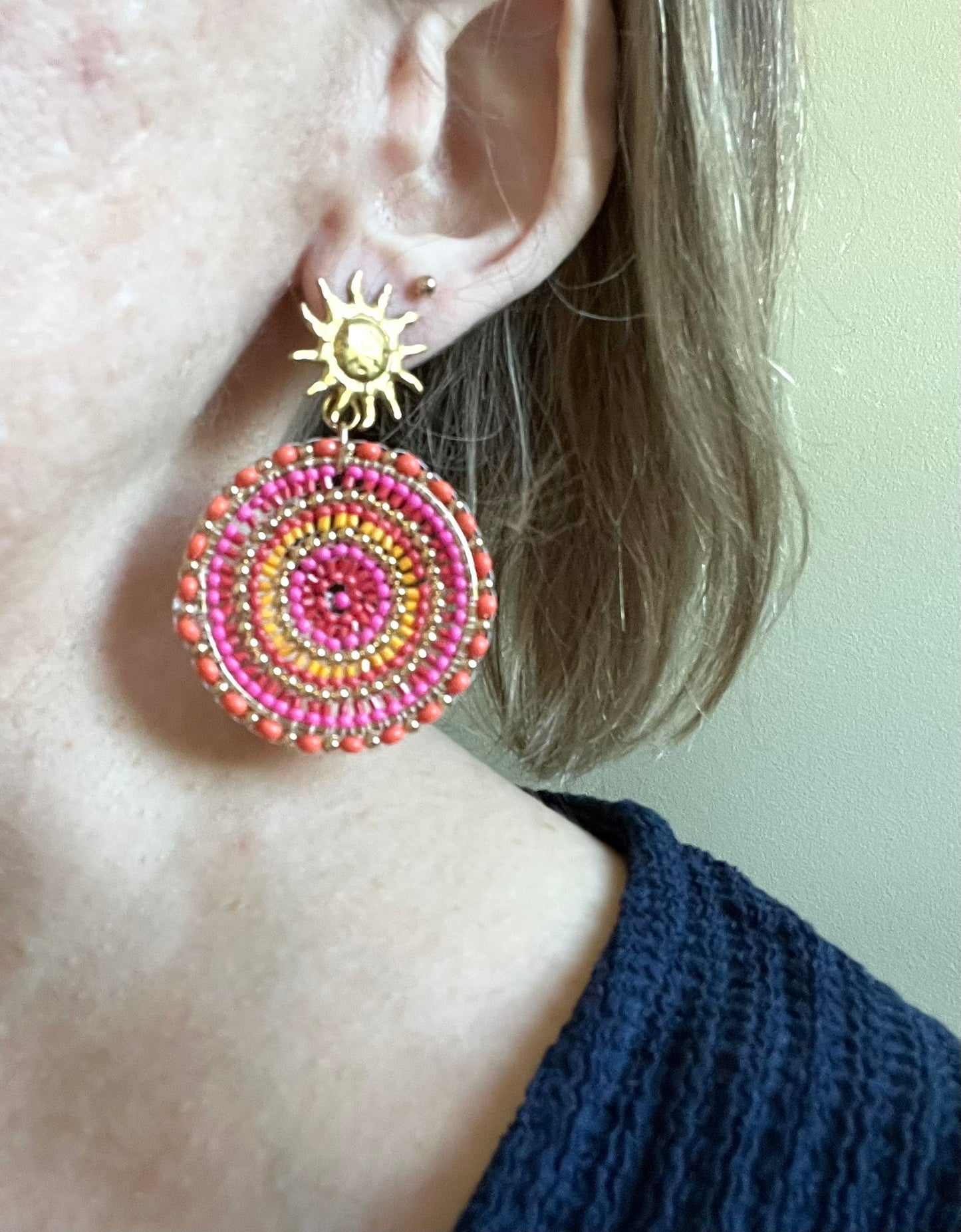 Boucles d'oreilles fantaisie fait main.
Clous d'oreilles soleil en acier doré.
Pendentif rond en perles de rocaille rose, orange.
Bijou fait main.