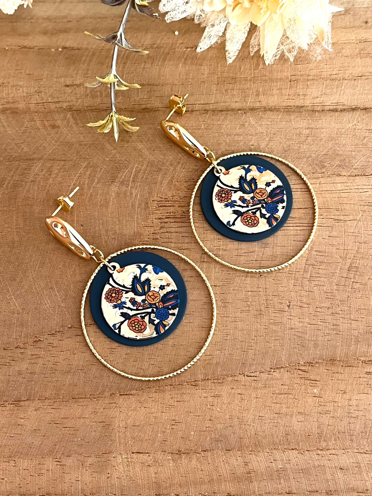 Boucles d'oreilles fantaisie fait main.
Clous d'oreilles martelés en laiton doré à l'or fin. Sequins ronds bleu marine, anneaux torsadés en laiton doré à l'or fin. Pendentif rond doré motif floral bleu et orange.
Bijou fantaisie fait main.