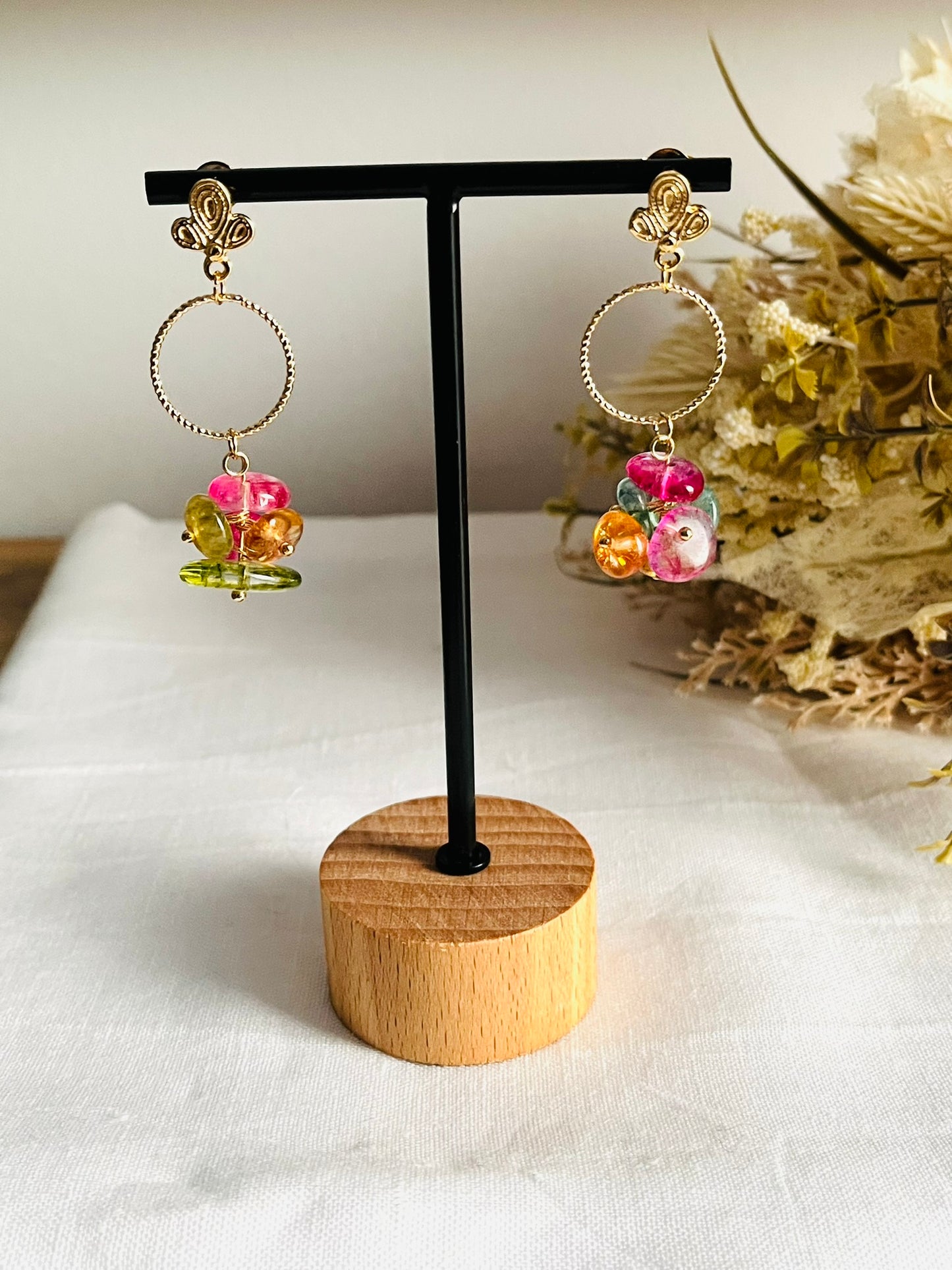 Boucles d'oreilles fantaisie fait main.
Clous d'oreilles feuille en laiton plaqué or 18k. Anneaux ciselés de 15mm en laiton plaqué or 18k. Grappe de perles en quartz coloré framboise,  vert olive, orange.
Bijou fantaisie fait main.