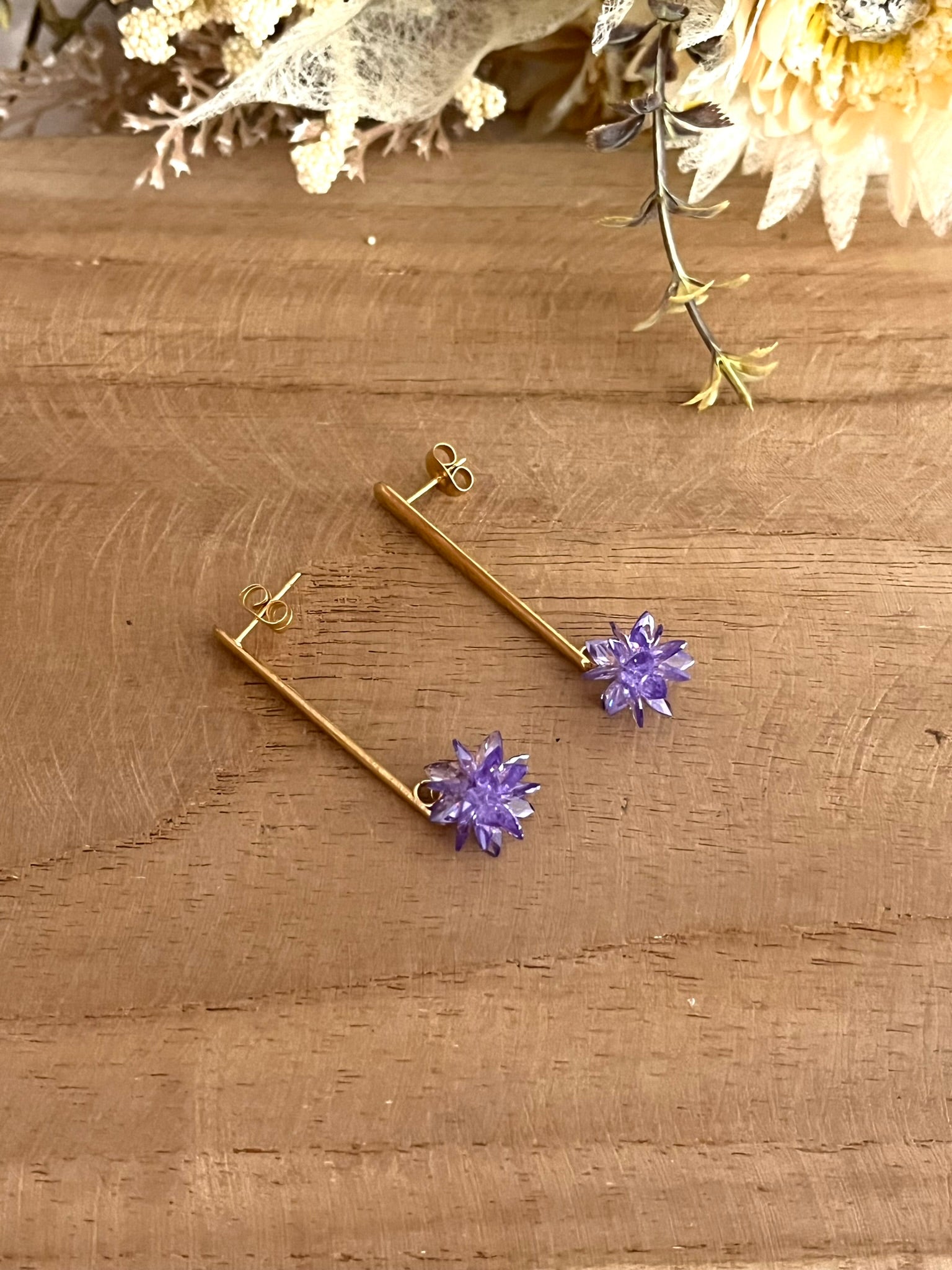 Boucles d'oreilles fantaisie fait main.
Clous d'oreilles longue barre en acier inoxydable doré. Pendentif fleur étoilée en verre cristal de couleur violet.
Bijou fantaisie fait main.