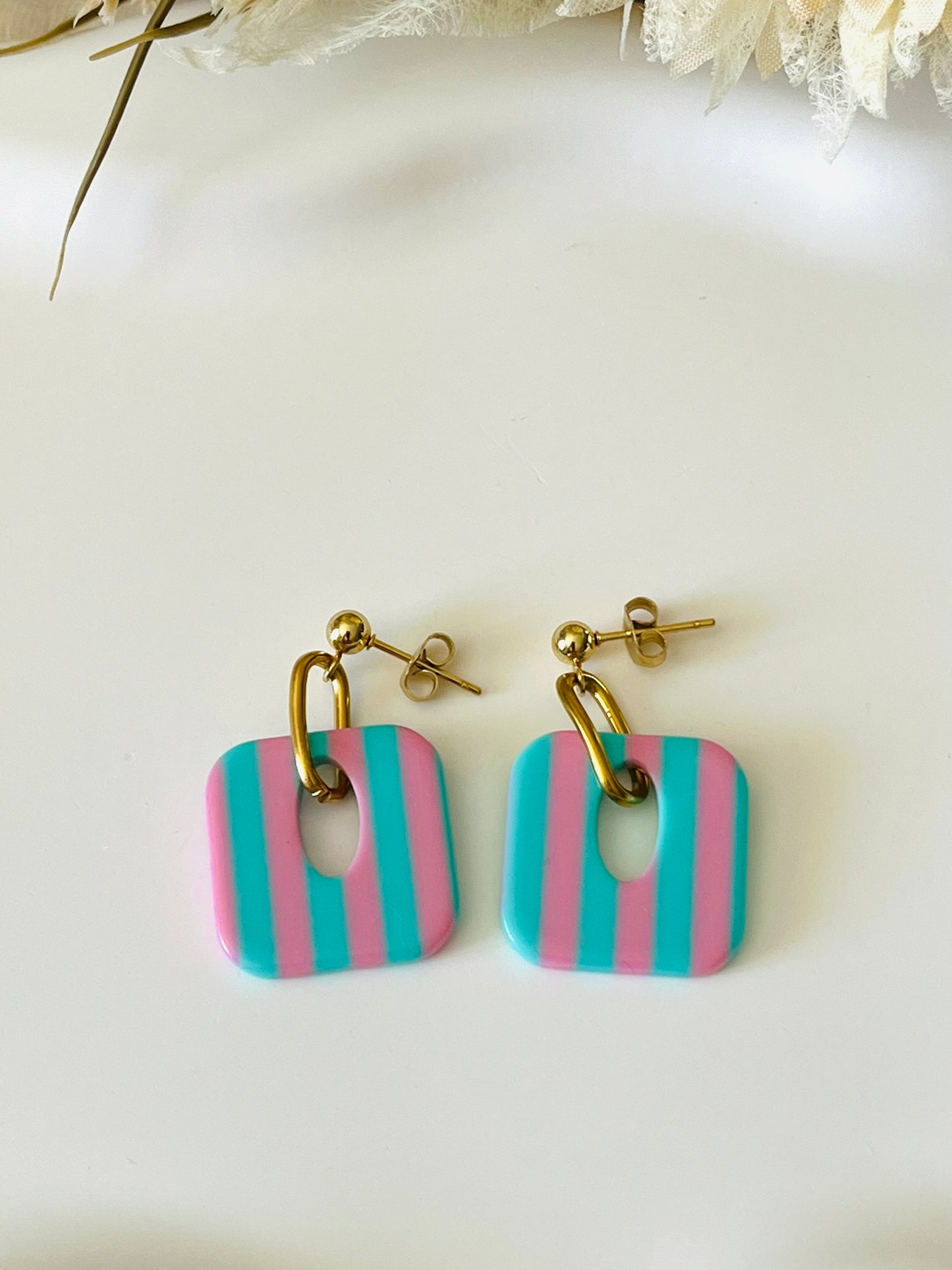 Boucles d'oreilles fantaisie fait main.
Clous d'oreilles en acier inoxydable doré. Pendentif carré en acrylique rayés.
Bijou fait main