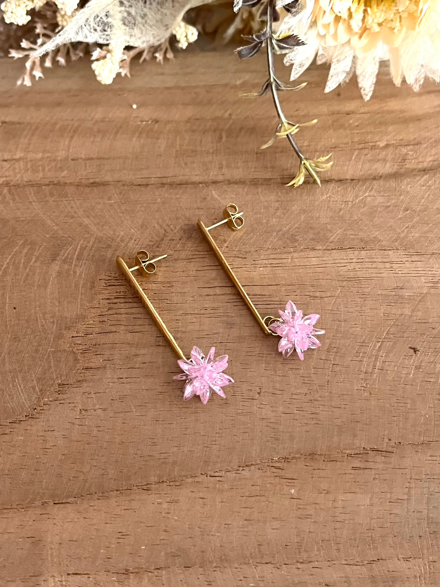 Boucles d'oreilles fantaisie fait main.
Clous d'oreilles longue barre en acier inoxydable doré. Pendentif fleur étoilée en verre cristal de couleur rose.
Bijou fantaisie fait main.