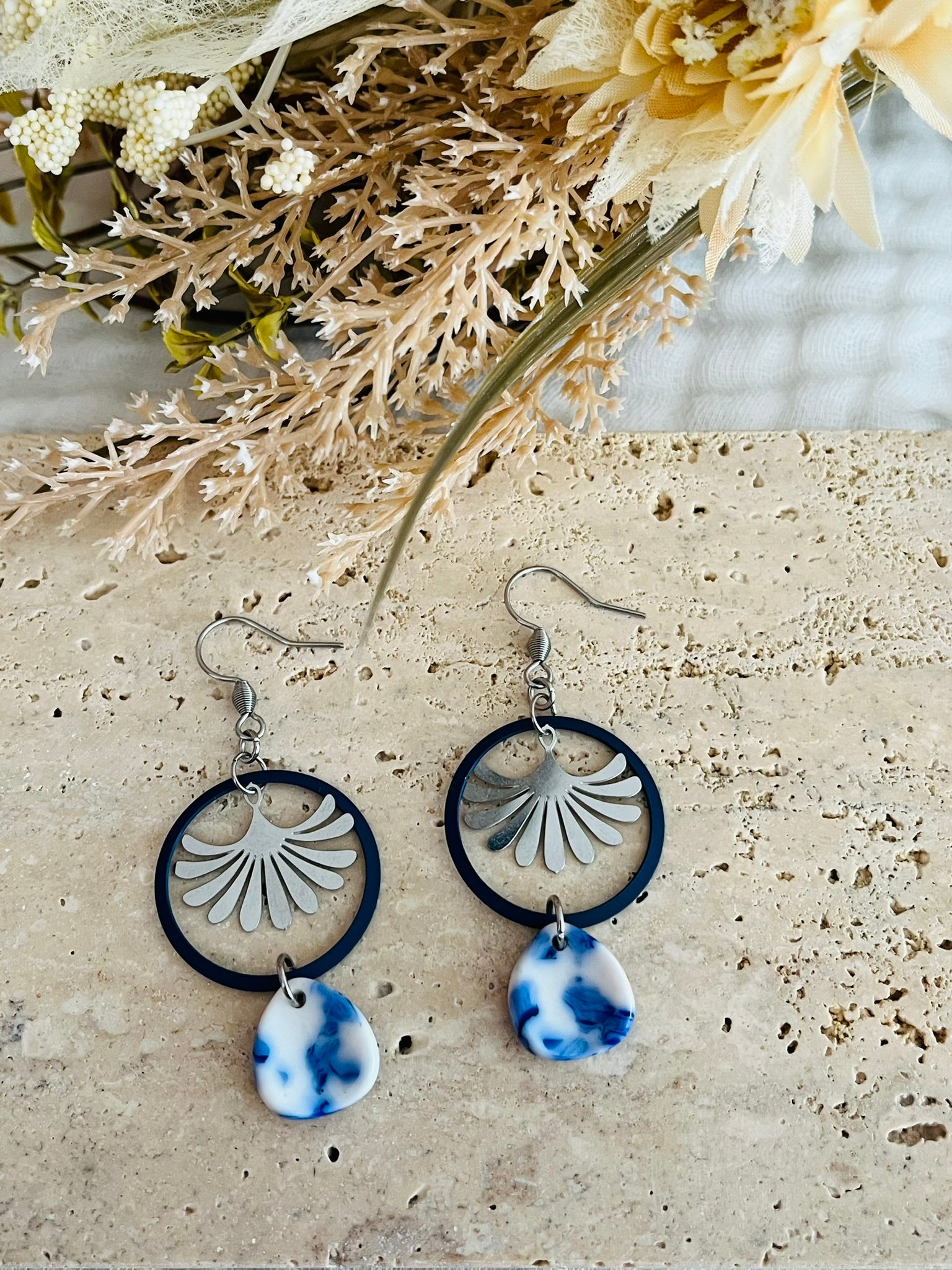 Boucles d'oreilles fantaisie fait main.
Crochets en acier inox, anneaux bleu marine, estampe éventail en acier inox, goutte en acrylique blanc marbré bleu.
Bijou fantaisie fait main.