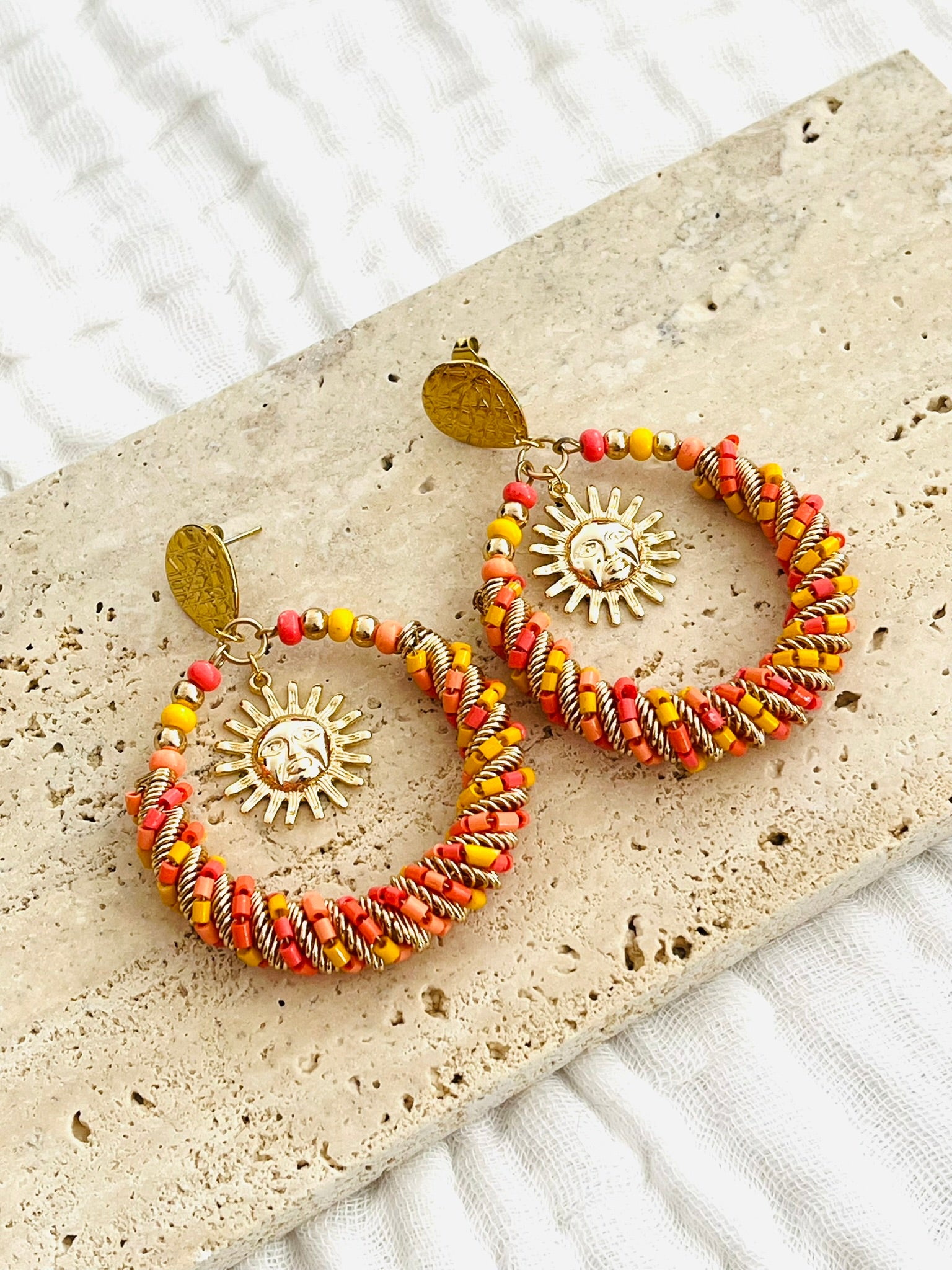 Boucles d'oreilles fantaisie fait main.
Clous d'oreilles goutte en acier doré.
Grand pendentif rond en perles de rocaille jaune, corail, rouge, orange.
Breloque soleil en laiton plaqué or 18k.
Bijou fait main.