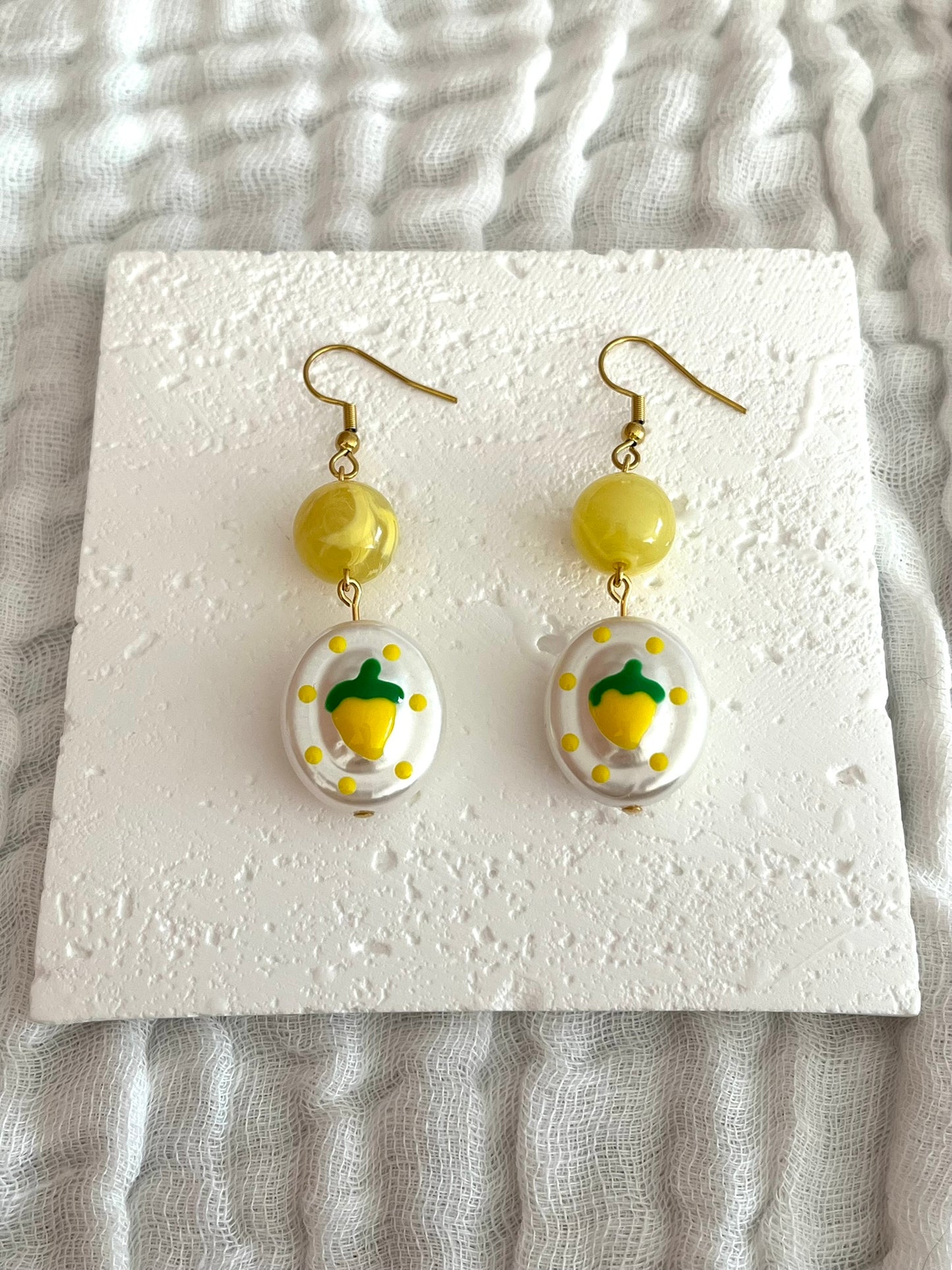 Boucles d'oreilles fantaisie fait main.
Crochets en acier inox doré. Perle ronde en acrylique jaune. Perle ovale en acrylique blanc nacré avec motif citron.
Bijou fantaisie fait main.