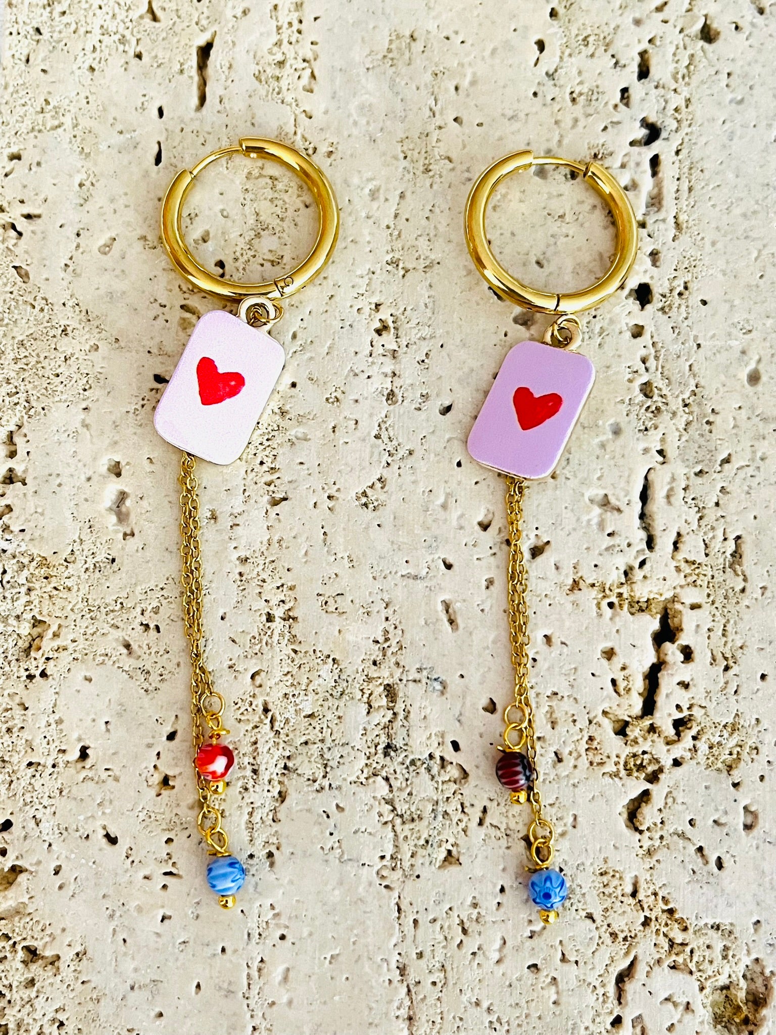 Boucles d'oreilles fantaisie fait main.
Créoles en acier doré.
Pendentif rectangle rose orné d'un coeur rouge.
2 Chainettes de longueur asymétrique réhaussées de perles millefiori dans les tons rouge et bleu.
Bijou fait main