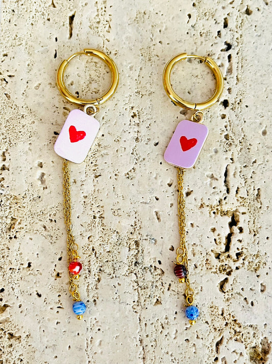 Boucles d'oreilles fantaisie fait main.
Créoles en acier doré.
Pendentif rectangle rose orné d'un coeur rouge.
2 Chainettes de longueur asymétrique réhaussées de perles millefiori dans les tons rouge et bleu.
Bijou fait main