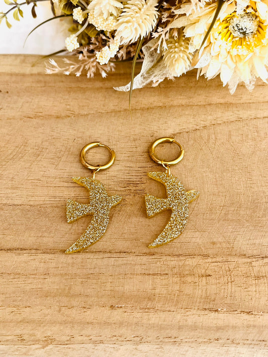 Boucles d'oreilles fantaisie fait main.
Créoles en acier inoxydable doré. Pendentifs hirondelle en acrylique doré pailleté.