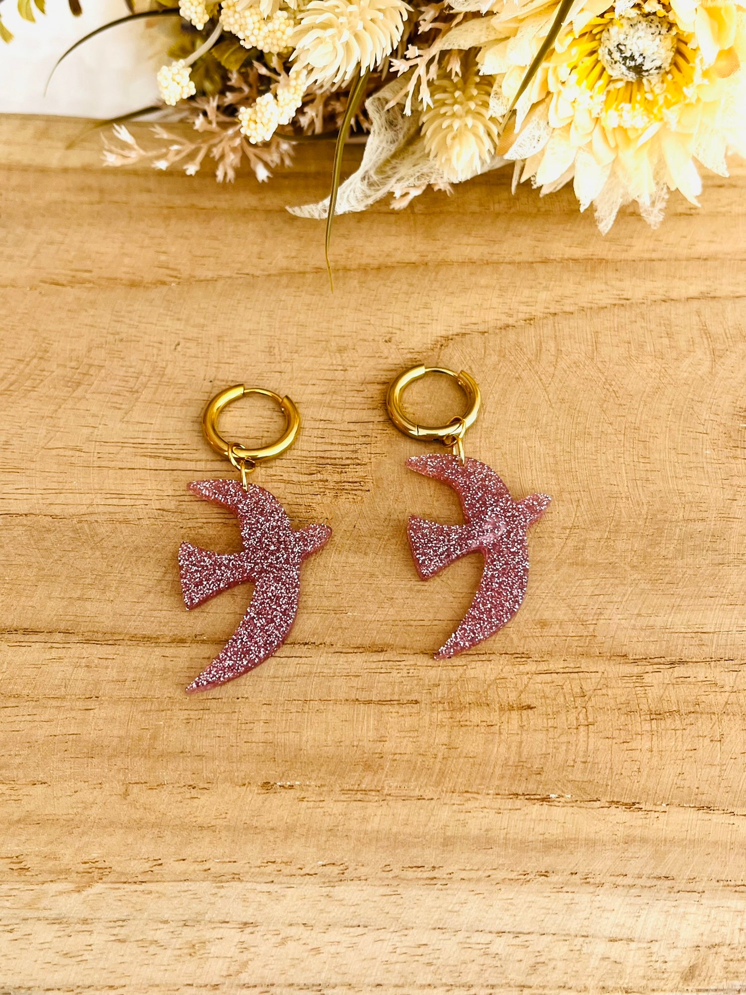 Boucles d'oreilles fantaisie fait main.
Créoles en acier inoxydable doré. Pendentifs hirondelle en acrylique rose pailleté.