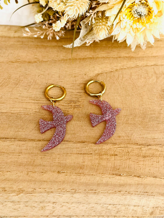 Boucles d'oreilles fantaisie fait main.
Créoles en acier inoxydable doré. Pendentifs hirondelle en acrylique rose pailleté.