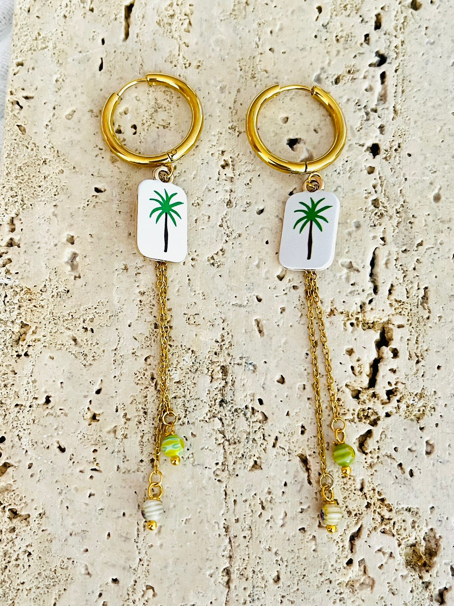 Boucles d'oreilles fantaisie fait main.
Créoles en acier doré.
Pendentif rectangle blanc orné d'un palmier vert.
2 Chainettes de longueur asymétrique réhaussées de perles millefiori dans les tons vert.
Bijou fait main