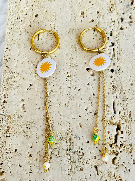 Boucles d'oreilles fantaisie fait main.
Créoles en acier doré.
Pendentif blanc blanc orné d'un soleil jaune.
2 Chainettes de longueur asymétrique réhaussées de perles millefiori dans les tons jaune et blanc.
Bijou fait main