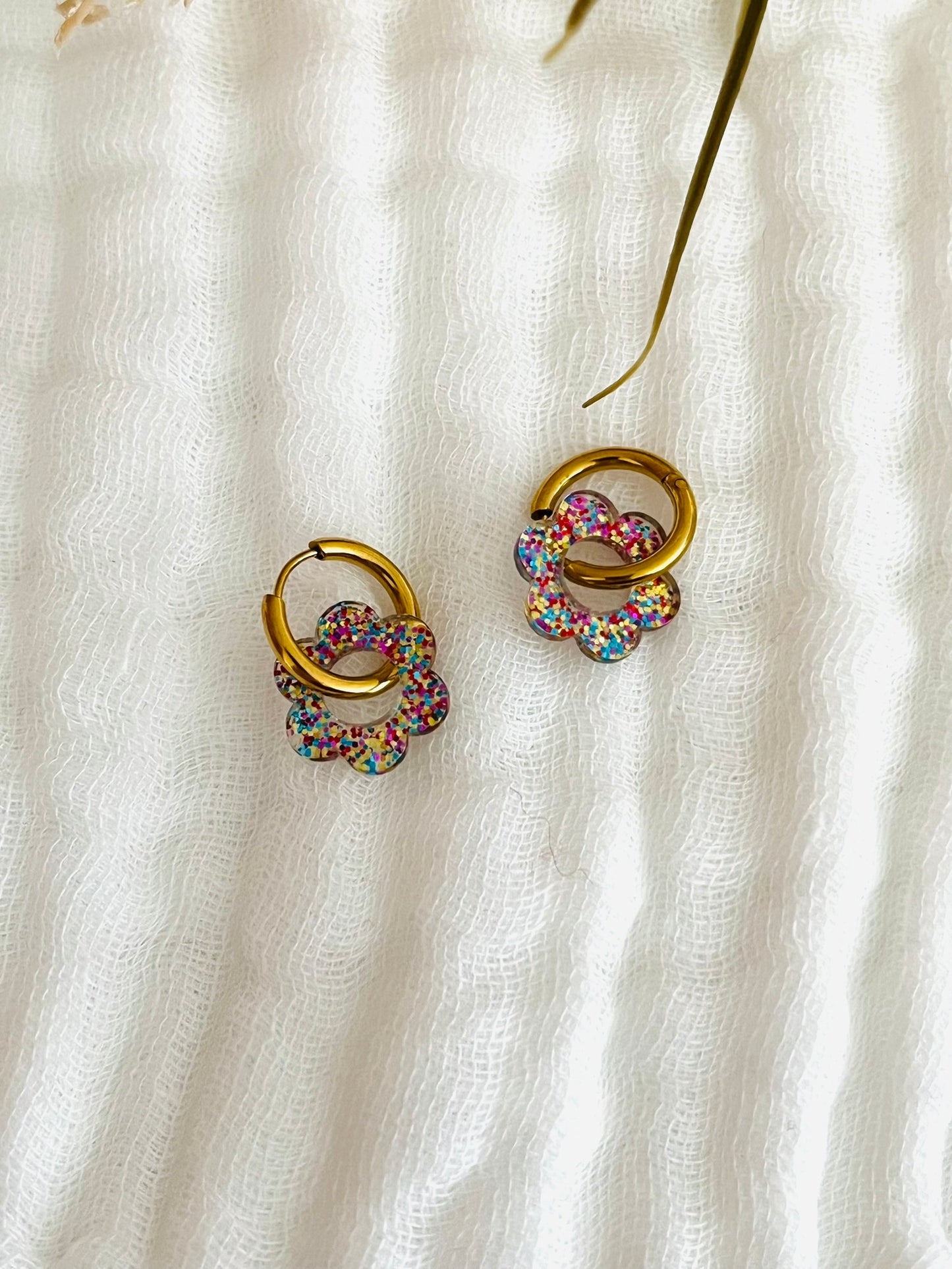 Boucles d'oreilles créoles adaptées pour les enfants à partir de 6 ans.
Créoles en acier inoxydable doré de 14mm.
Petites fleurs multicolore pailleté en acrylique.