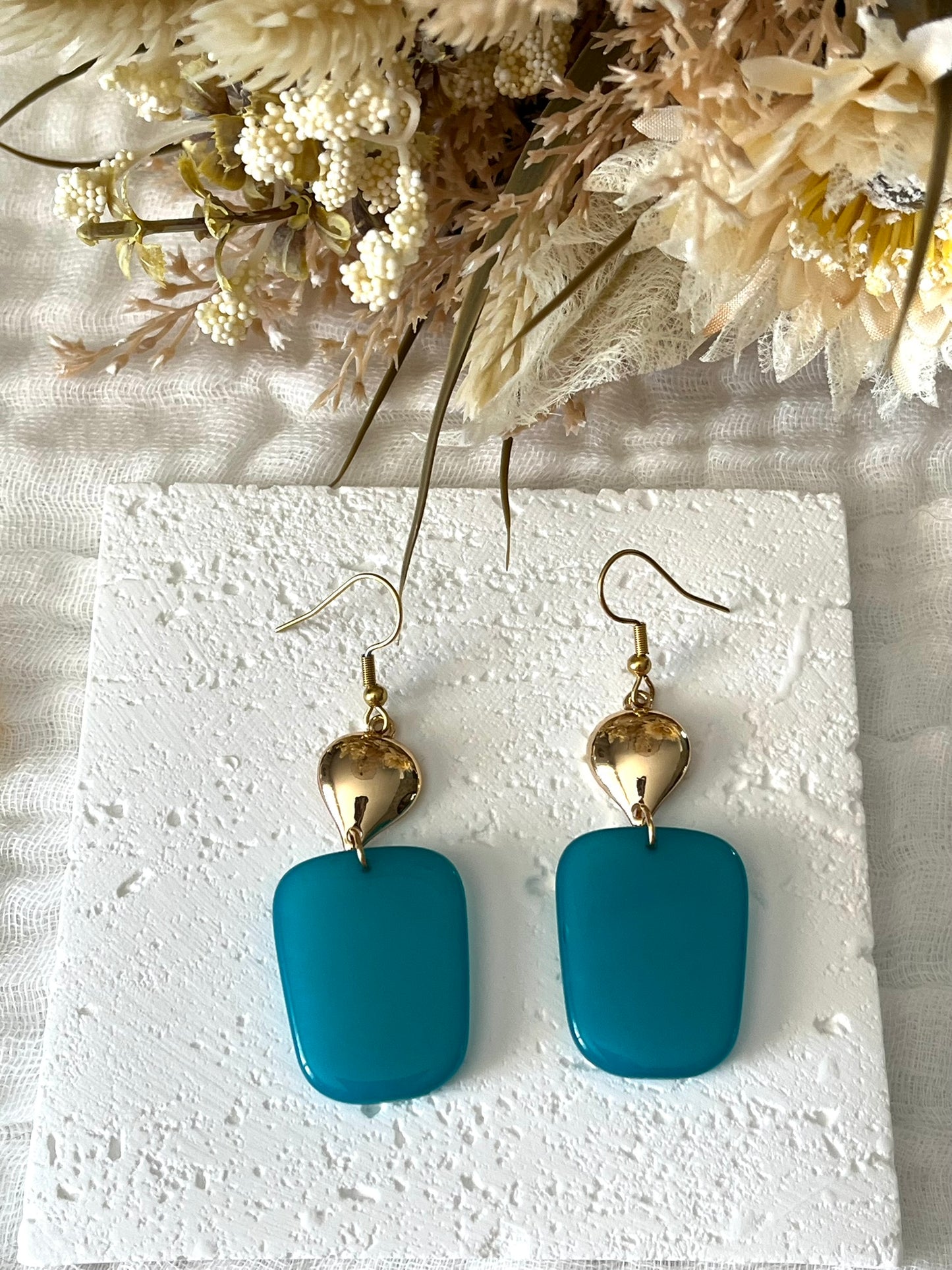 Boucles d'oreilles fantaisie fait main.
Crochets en acier inox doré.
Connecteurs goutte dorés.
Pendentifs trapèze en résine bleu lagune.
Bijou fantaisie fait main.