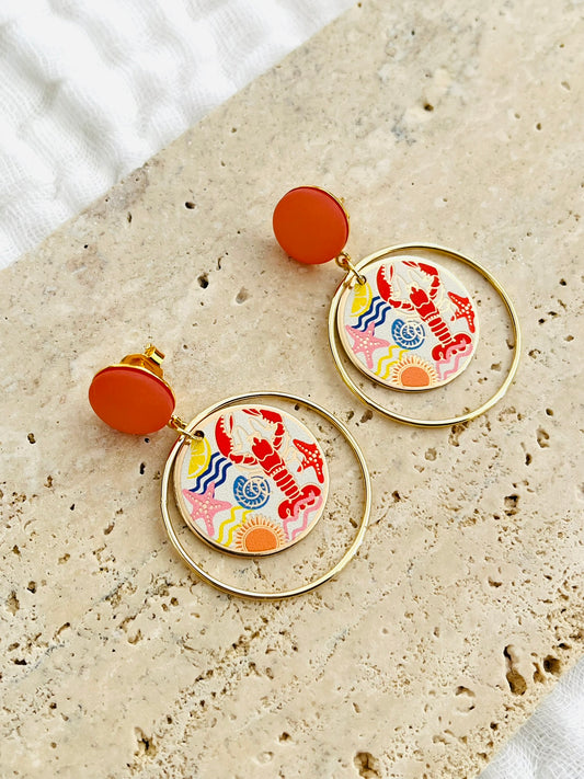 Boucles d'oreilles fantaisie fait main.
Clous d'oreilles en laiton doré à l'or fin rehaussé d'un cabochon corail.
Anneaux fermés en laiton plaqué or 18k.
Pendentifs ronds imprimé homard, étoile de mer, coquillage, soleil.
Bijou fait main.