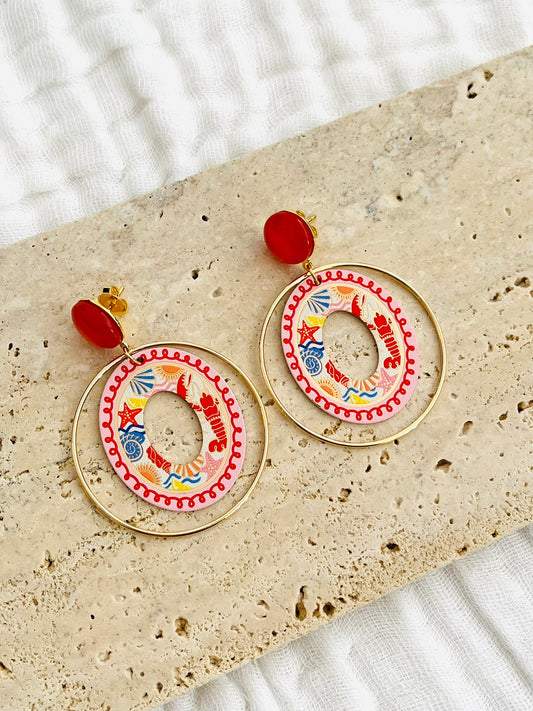 Boucles d'oreilles fantaisie fait main.
Clous d'oreilles en laiton doré à l'or fin rehaussé d'un cabochon rouge.
Anneaux fermés en laiton plaqué or 18k.
Pendentifs ronds imprimé homard, étoile de mer, coquillage, soleil.
Bijou fait main.
