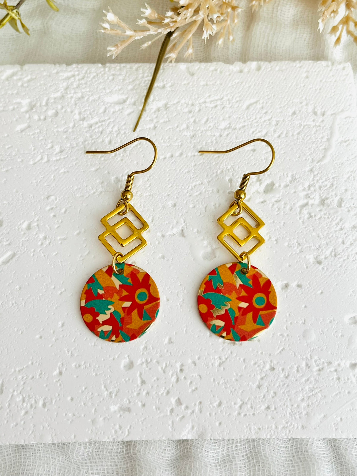 Boucles d'oreilles fantaisie fait main.
Style géométrique avec médaillon rond motif fleurs orange, vert, jaune.
En acier inoxydable.
Bijou fait main