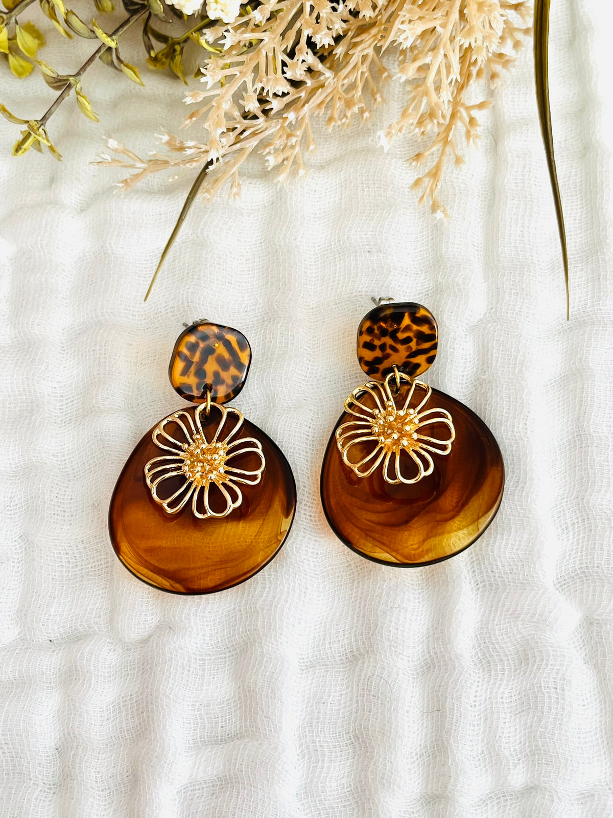 Boucles d'oreilles fantaisie fait main.
Clous d'oreilles carrée en acrylique motif léopard marron et noir; pendentifs en acrylique forme pétale marron ambré; pendentifs fleur ajourée en laiton or 18k.
Bijou fait main.