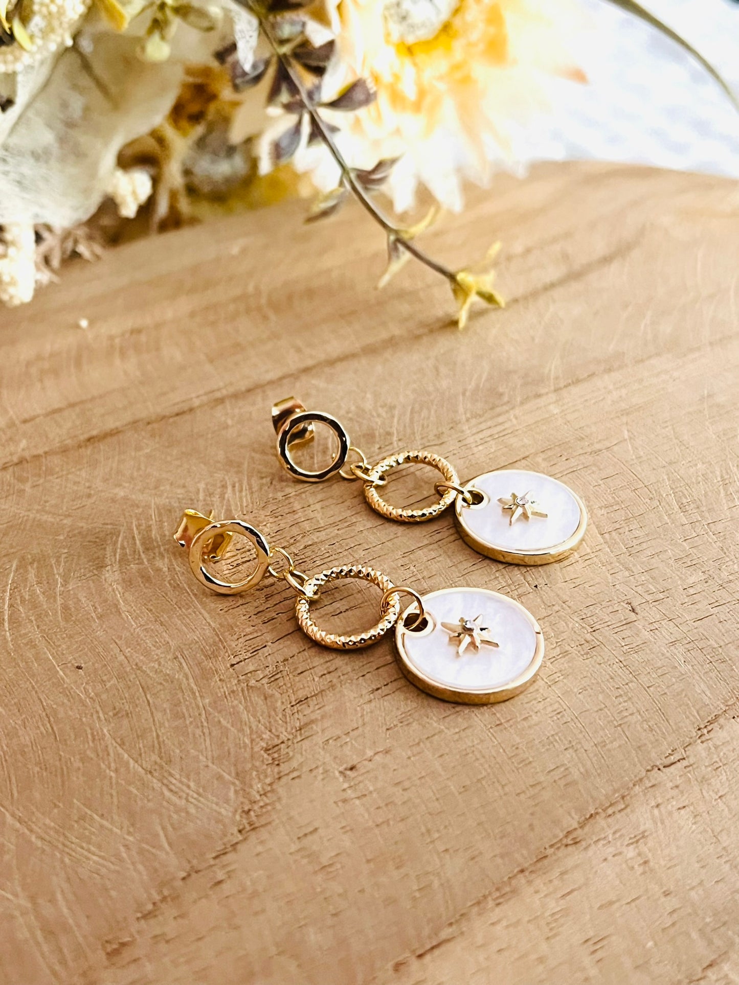 Boucles d'oreilles fantaisie fait main.
Clous d'oreilles cercle en laiton plaqué or 18k. Pendentif en nacre avec étoile polaire serti d'un strass.
Bijou fantaisie fait main.