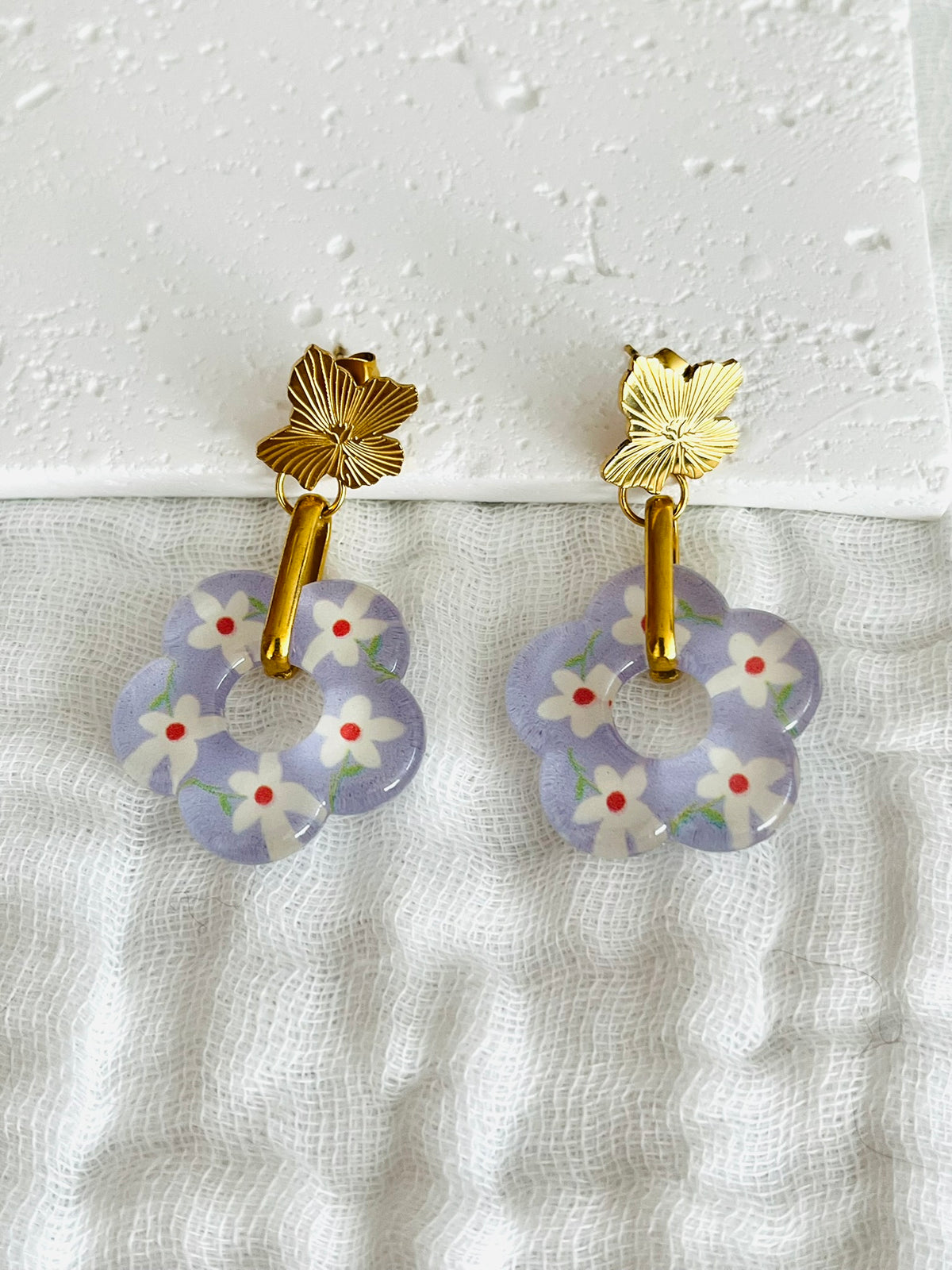 Boucles d'oreilles fantaisie faites main.
Clous d'oreilles fleur en acier inox doré, anneaux ovales en acier doré, pendentif fleur en acrylique violet lilas avec petites fleurs blanches.
Bijou fait main.
