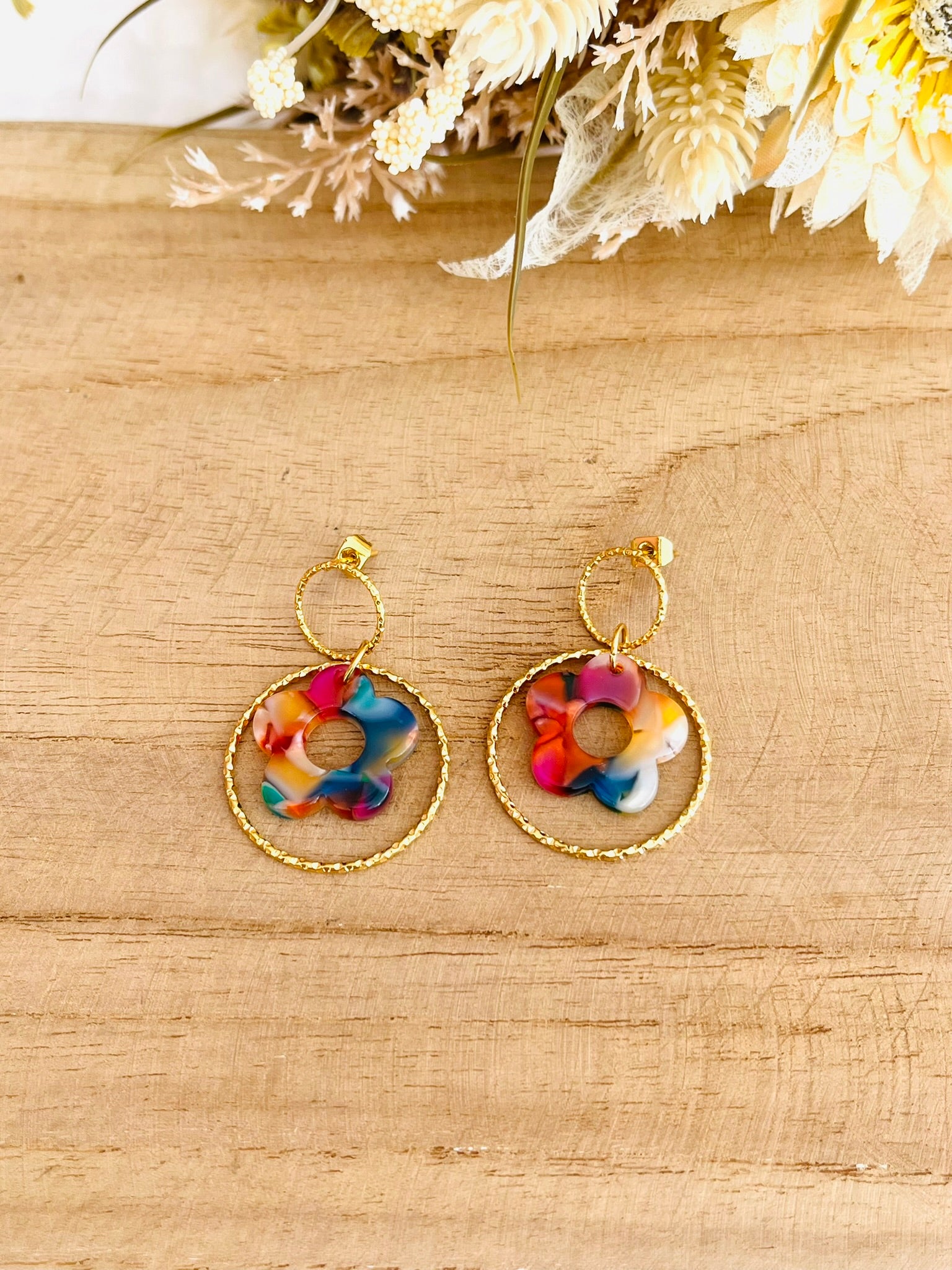 Boucles d'oreilles fantaisie fait main.
Clous d'oreilles ronds en acier inox doré, anneau fermé ciselé en acier doré, fleur multicolore en acrylique.
Bijou fantaisie fait main.