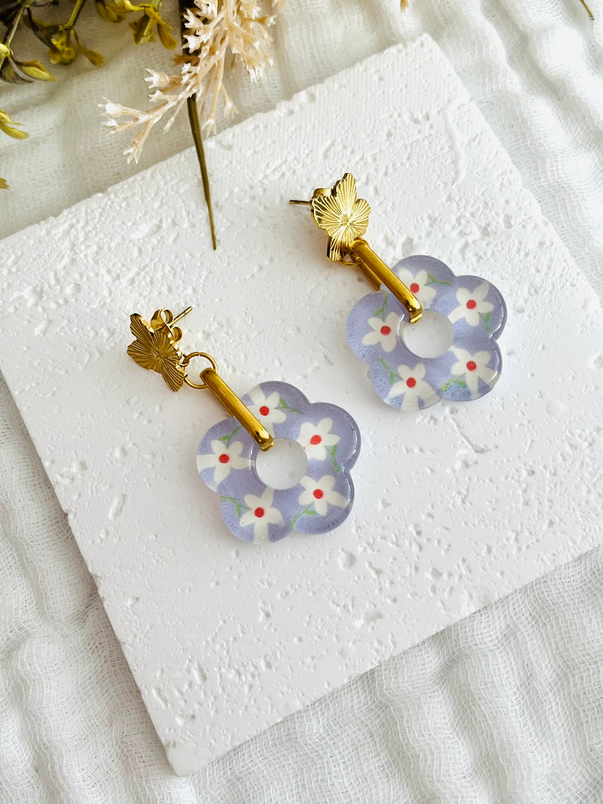 Boucles d'oreilles fantaisie faites main.
Clous d'oreilles fleur en acier inox doré, anneaux ovales en acier doré, pendentif fleur en acrylique violet lilas avec petites fleurs blanches.
Bijou fait main.