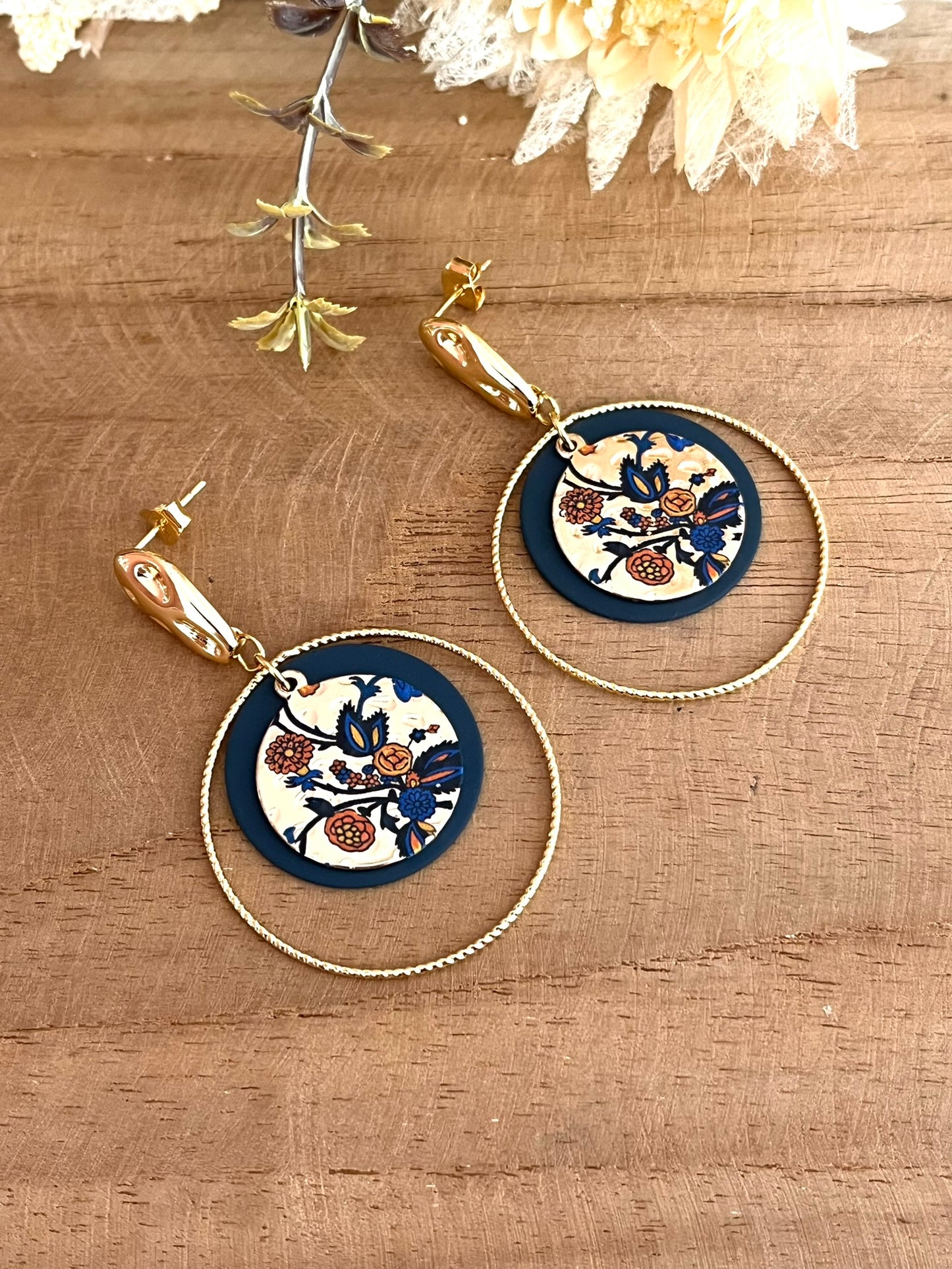 Boucles d'oreilles fantaisie fait main.
Clous d'oreilles martelés en laiton doré à l'or fin. Sequins ronds bleu marine, anneaux torsadés en laiton doré à l'or fin. Pendentif rond doré motif floral bleu et orange.
Bijou fantaisie fait main.