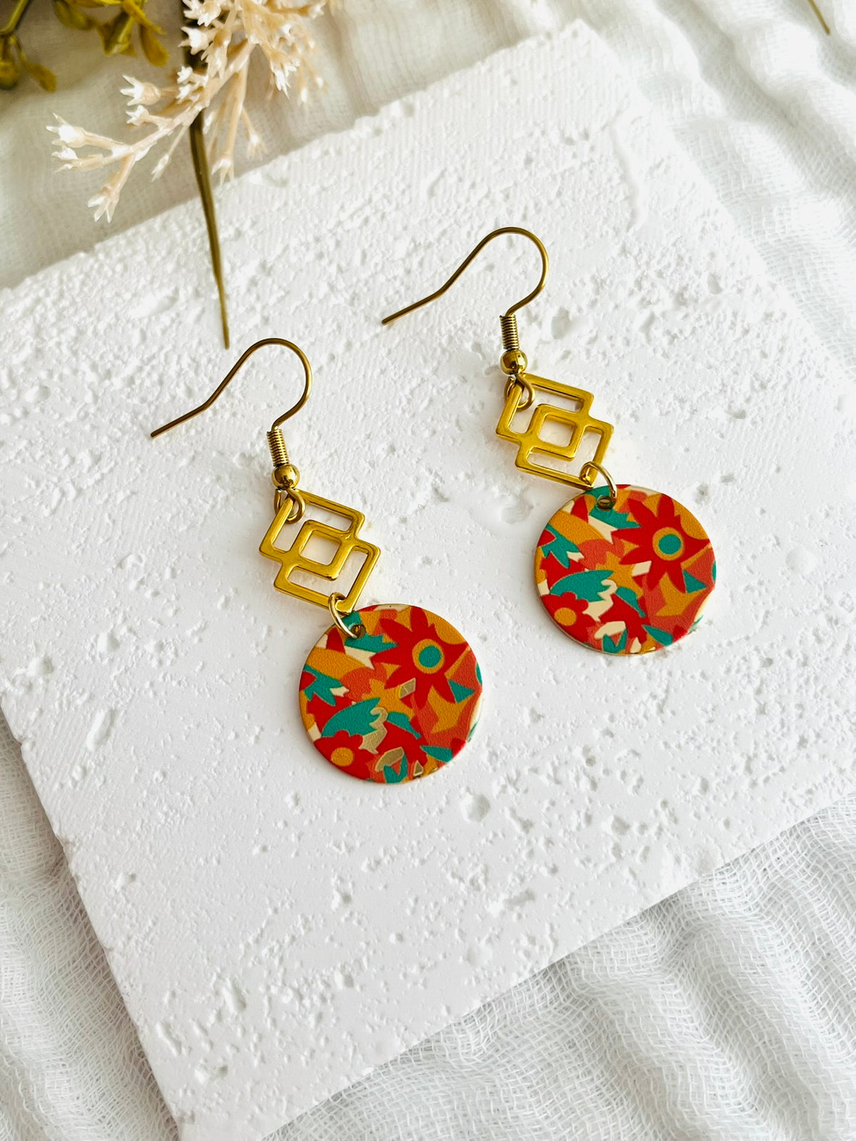 Boucles d'oreilles fantaisie fait main.
Style géométrique avec médaillon rond motif fleurs orange, vert, jaune.
En acier inoxydable.
Bijou fait main