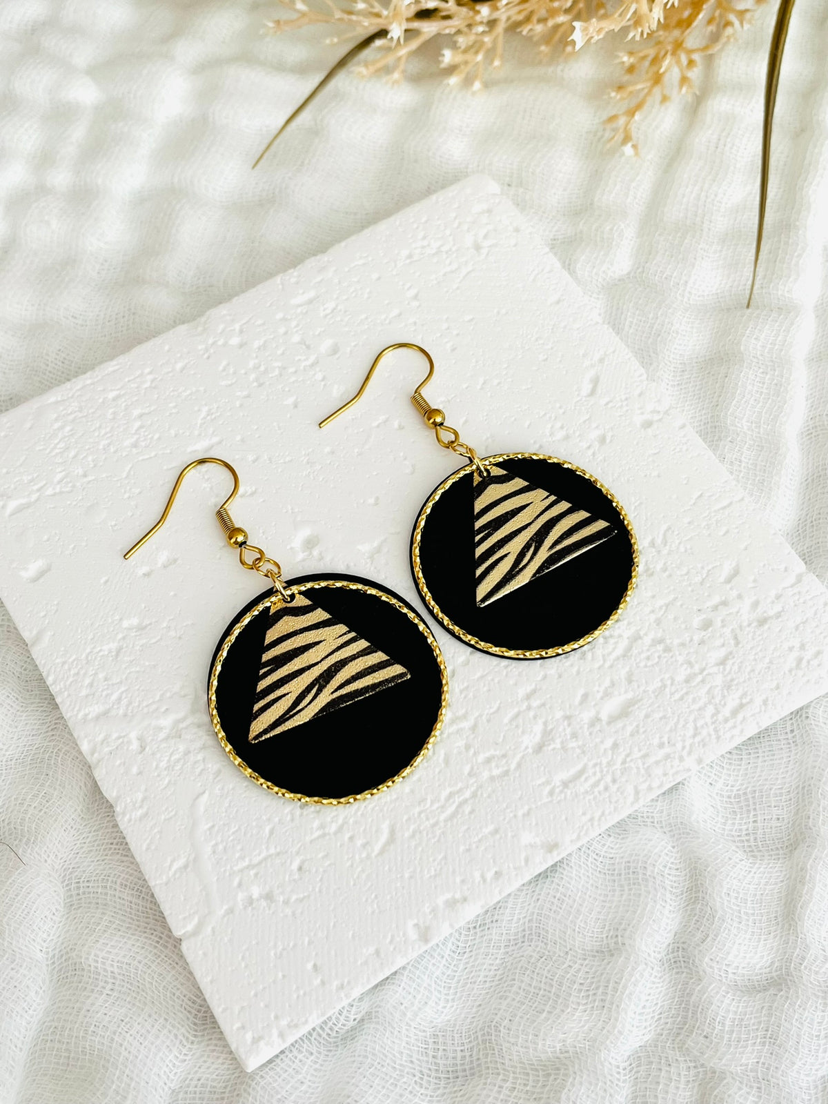 Boucles d'oreilles fantaisie fait main.
Crochets d'oreilles en acier inox doré; anneaux fermés ciselés or 18k; pendentif disque noir; sequin triangle motif zèbre noir et or pailleté.
Bijou fait main.