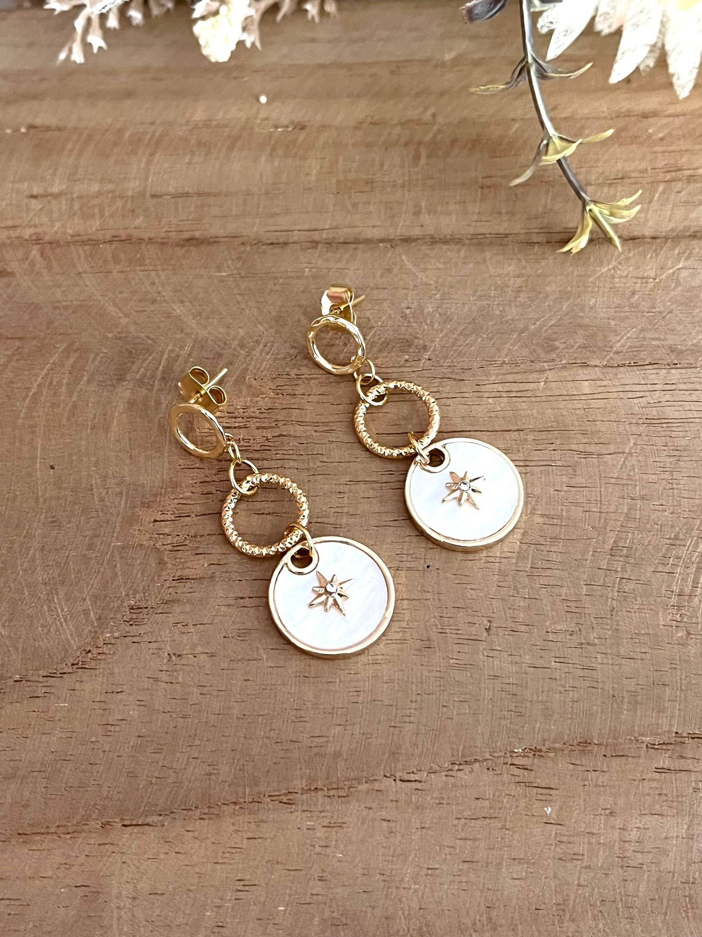 Boucles d'oreilles fantaisie fait main.
Clous d'oreilles cercle en laiton plaqué or 18k. Pendentif en nacre avec étoile polaire serti d'un strass.
Bijou fantaisie fait main.