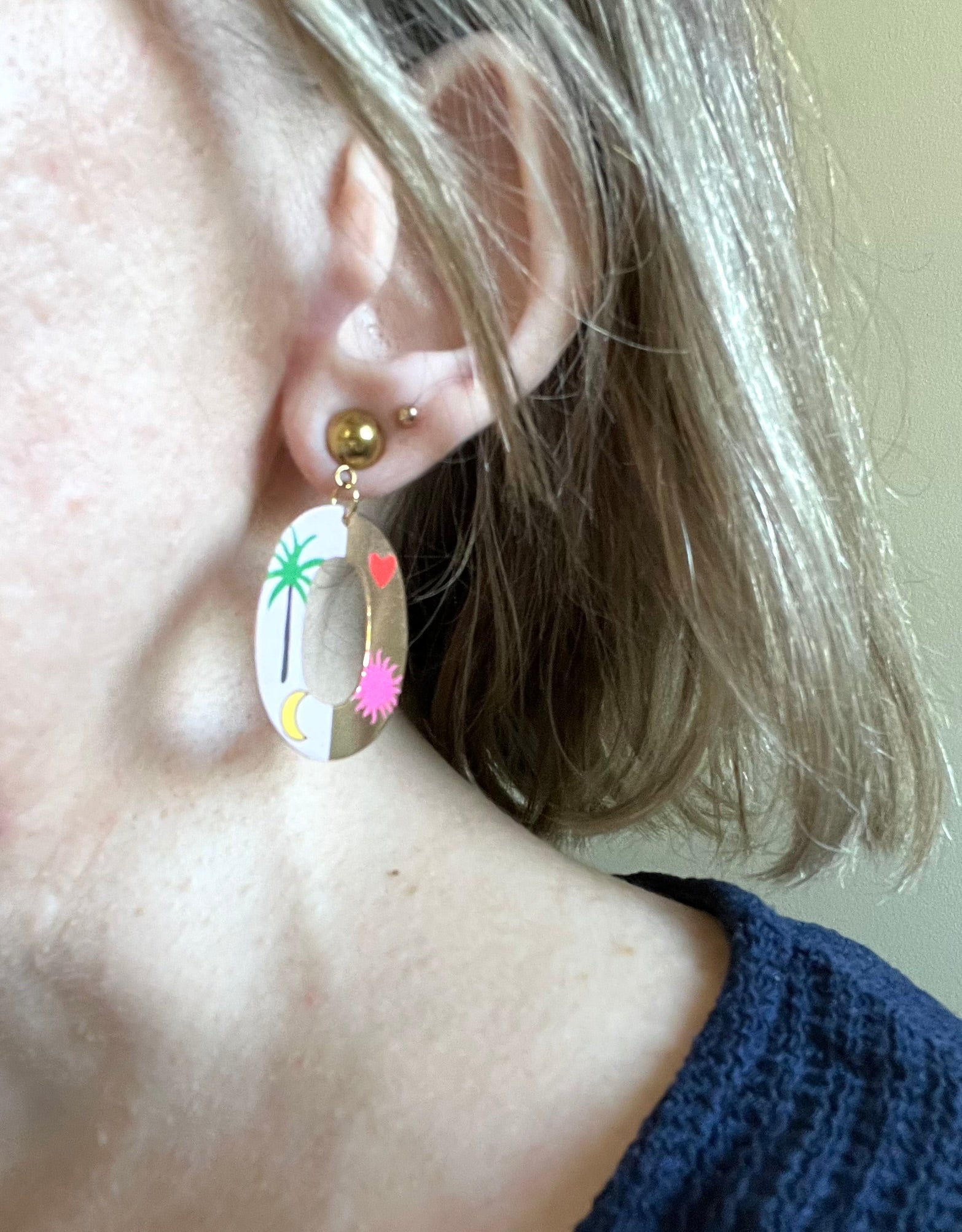 Boucles d'oreilles fantaisie fait main.
Clous d'oreilles en acier inox doré.
Pendentif ovale doré et rose avec motif palmier, soleil, lune, coeur.
Bijou fait main.