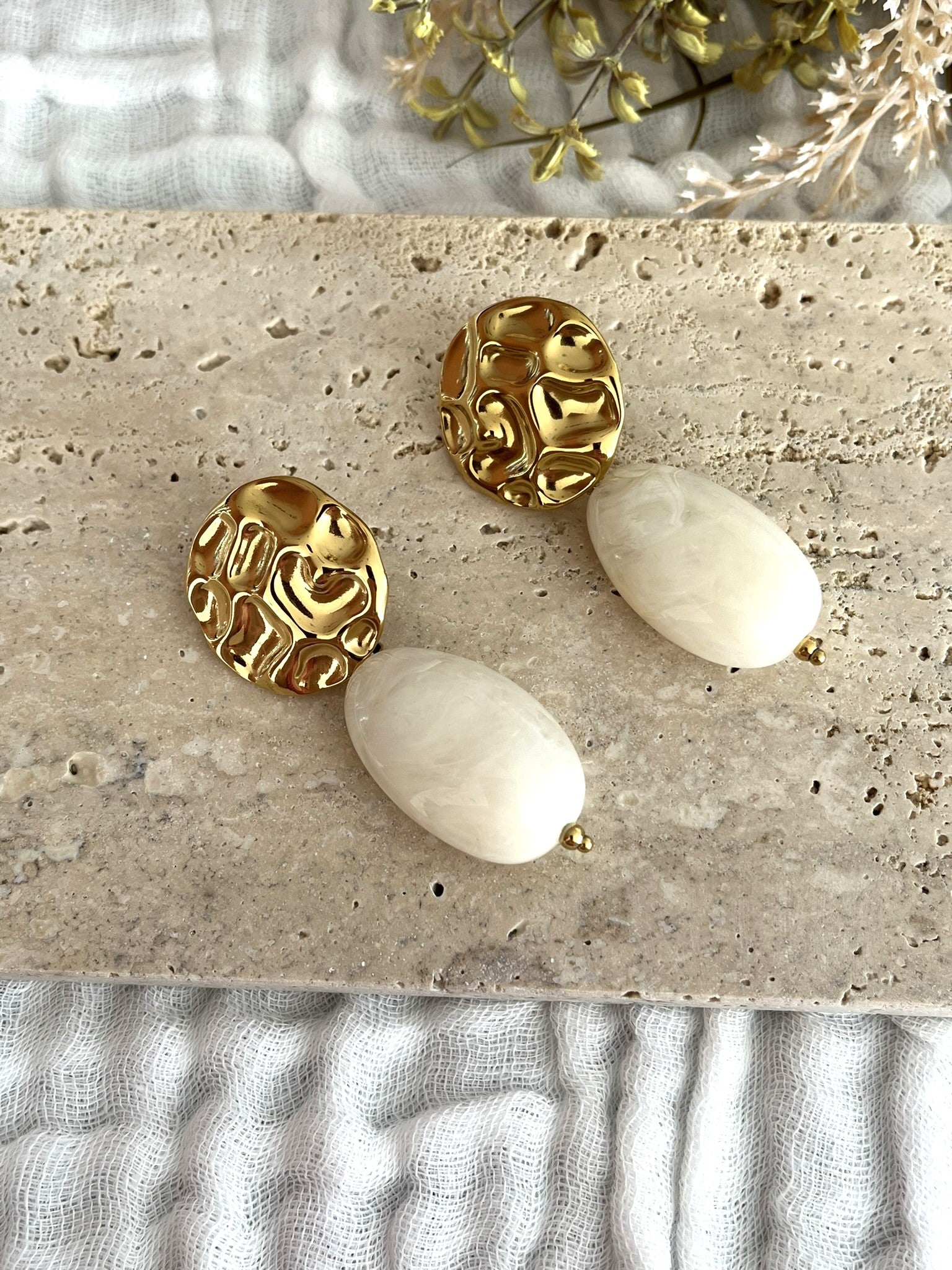 Boucles d'oreilles fantaisie fait main.
Clous d'oreilles ronds martelés en acier inoxydable doré.
Perle ovale en résine blanc cassé marbré.
Bijou fantaisie fait main.
