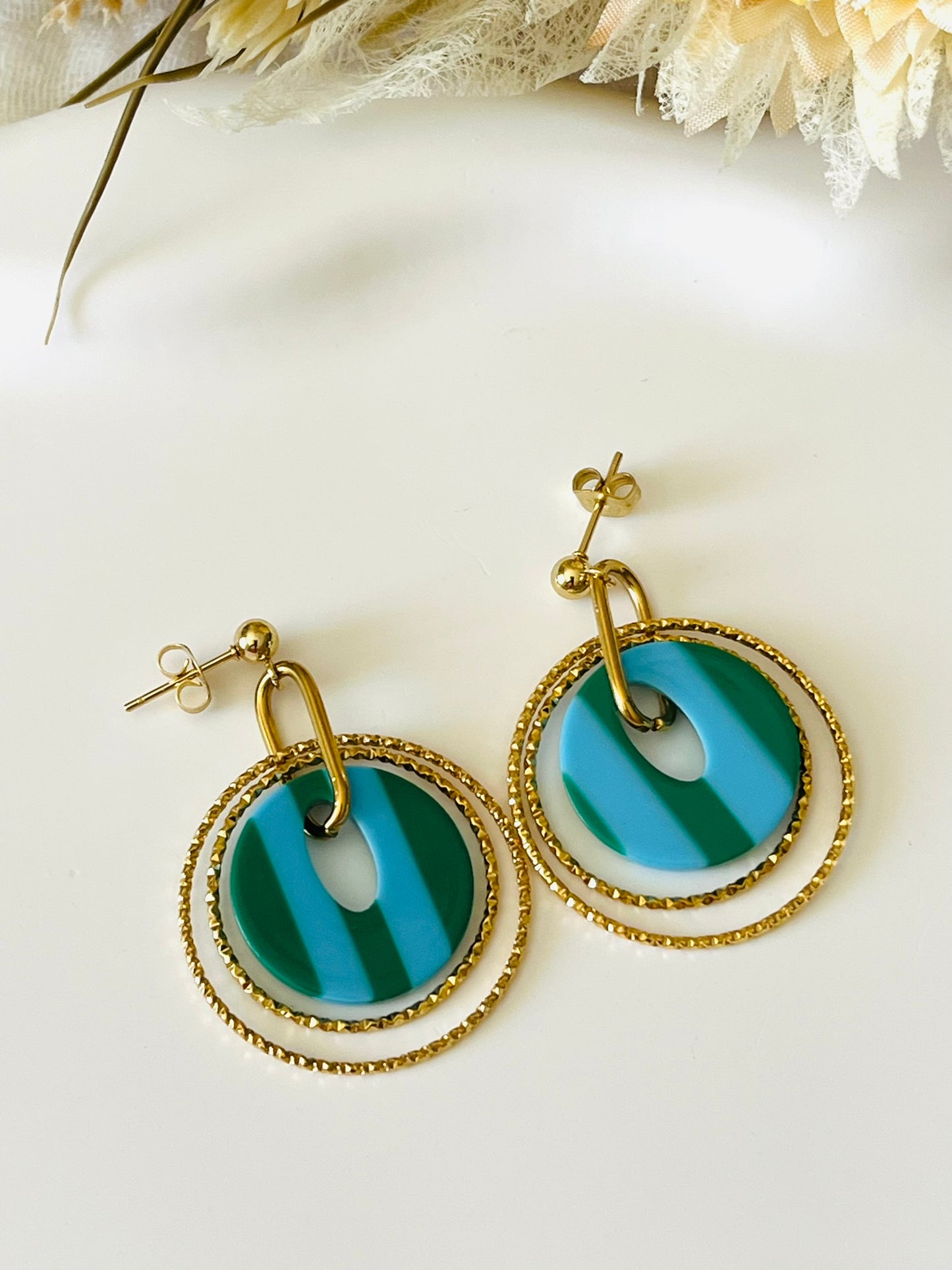 Boucles d'oreilles fantaisie fait main.
Clous d'oreilles en acier doré.
Jeu d'anneaux ciselés de 25 et 30mm en acier doré.
Pendentifs ronds en acrylique rayés bleu et vert.
Bijou fantaisie fait main.