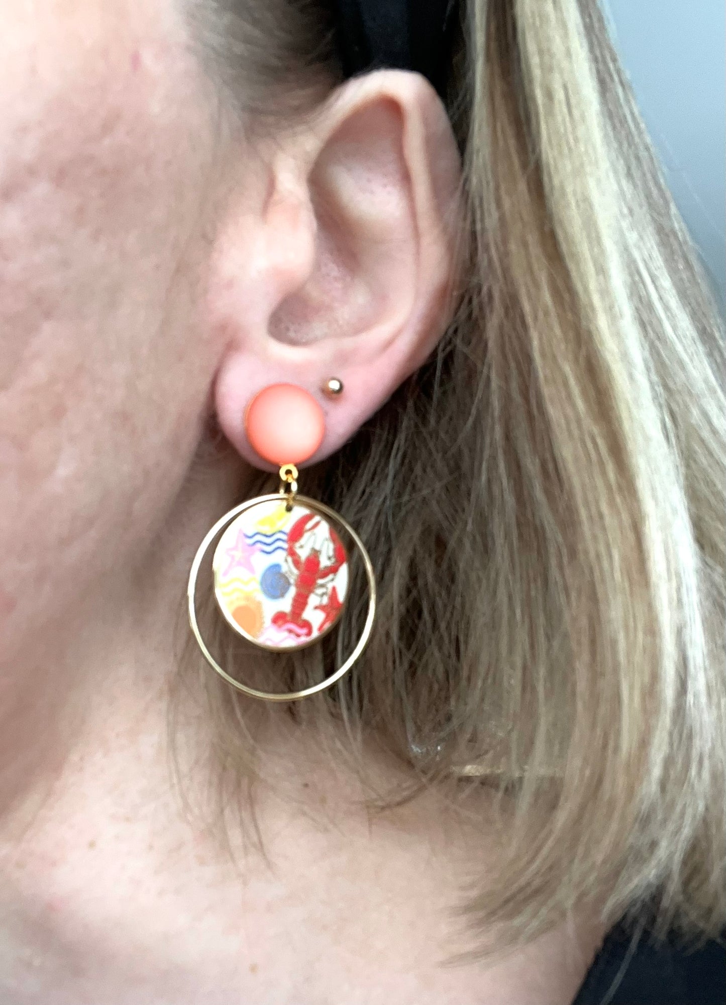 Boucles d'oreilles fantaisie fait main.
Clous d'oreilles en laiton doré à l'or fin rehaussé d'un cabochon corail.
Anneaux fermés en laiton plaqué or 18k.
Pendentifs ronds imprimé homard, étoile de mer, coquillage, soleil.
Bijou fait main.