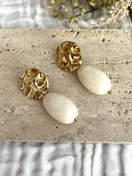 Boucles d'oreilles fantaisie fait main.
Clous d'oreilles ronds martelés en acier inoxydable doré.
Perle ovale en résine blanc cassé marbré.
Bijou fantaisie fait main.