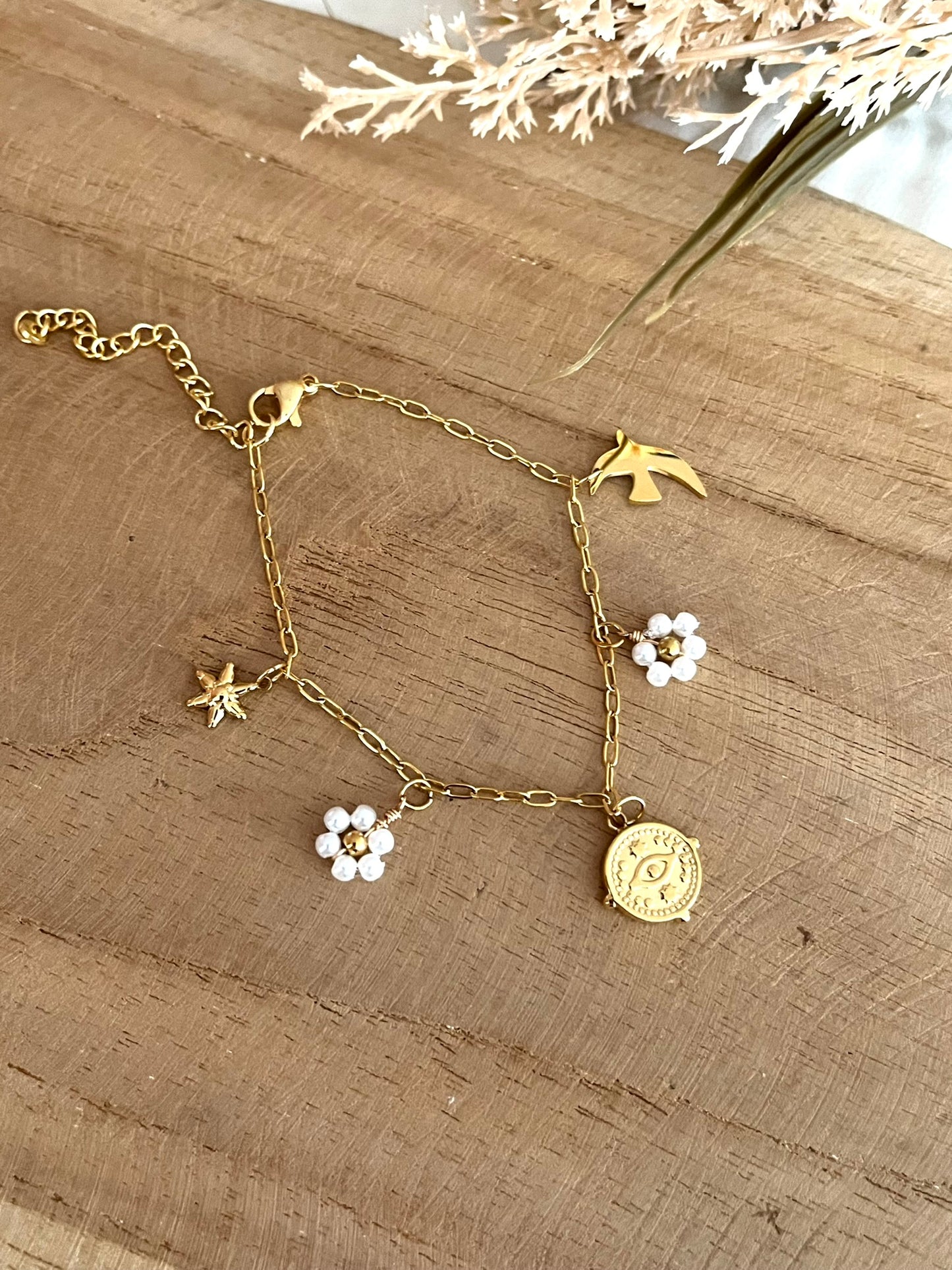 Bracelet fantaisie fait main.
Bracelet à charms en acier inoxydable doré orné de fleurs perlées blanc nacré, une hirondelle, une étoile et une breloque oeil protecteur en acier doré.
Bijou fantaisie fait main.