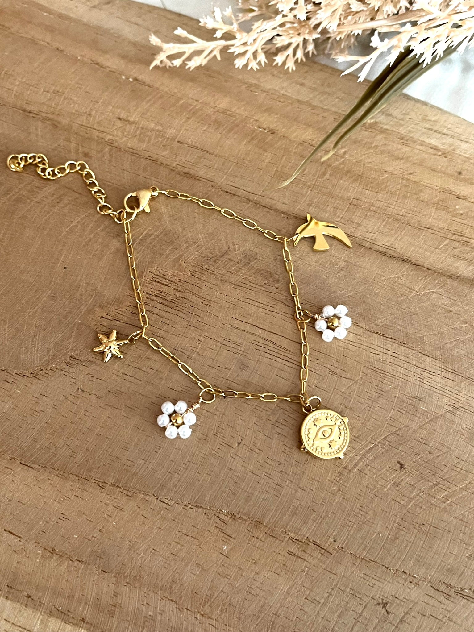 Bracelet fantaisie fait main.
Bracelet à charms en acier inoxydable doré orné de fleurs perlées blanc nacré, une hirondelle, une étoile et une breloque oeil protecteur en acier doré.
Bijou fantaisie fait main.