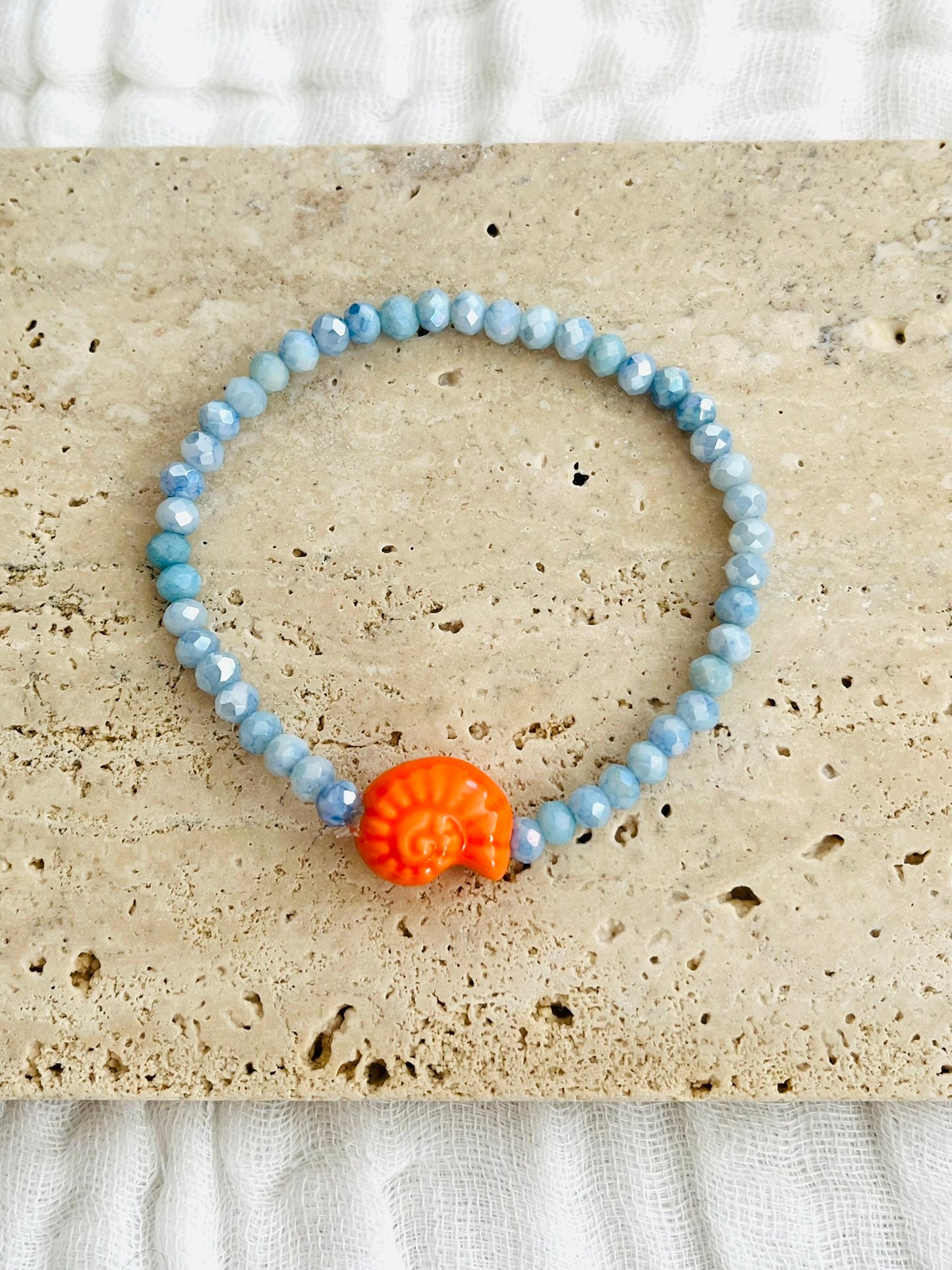 Bracelet élastique fait main.
Perles en verre facettées bleu et perle coquillage en céramique orange.
Bijou fait main.