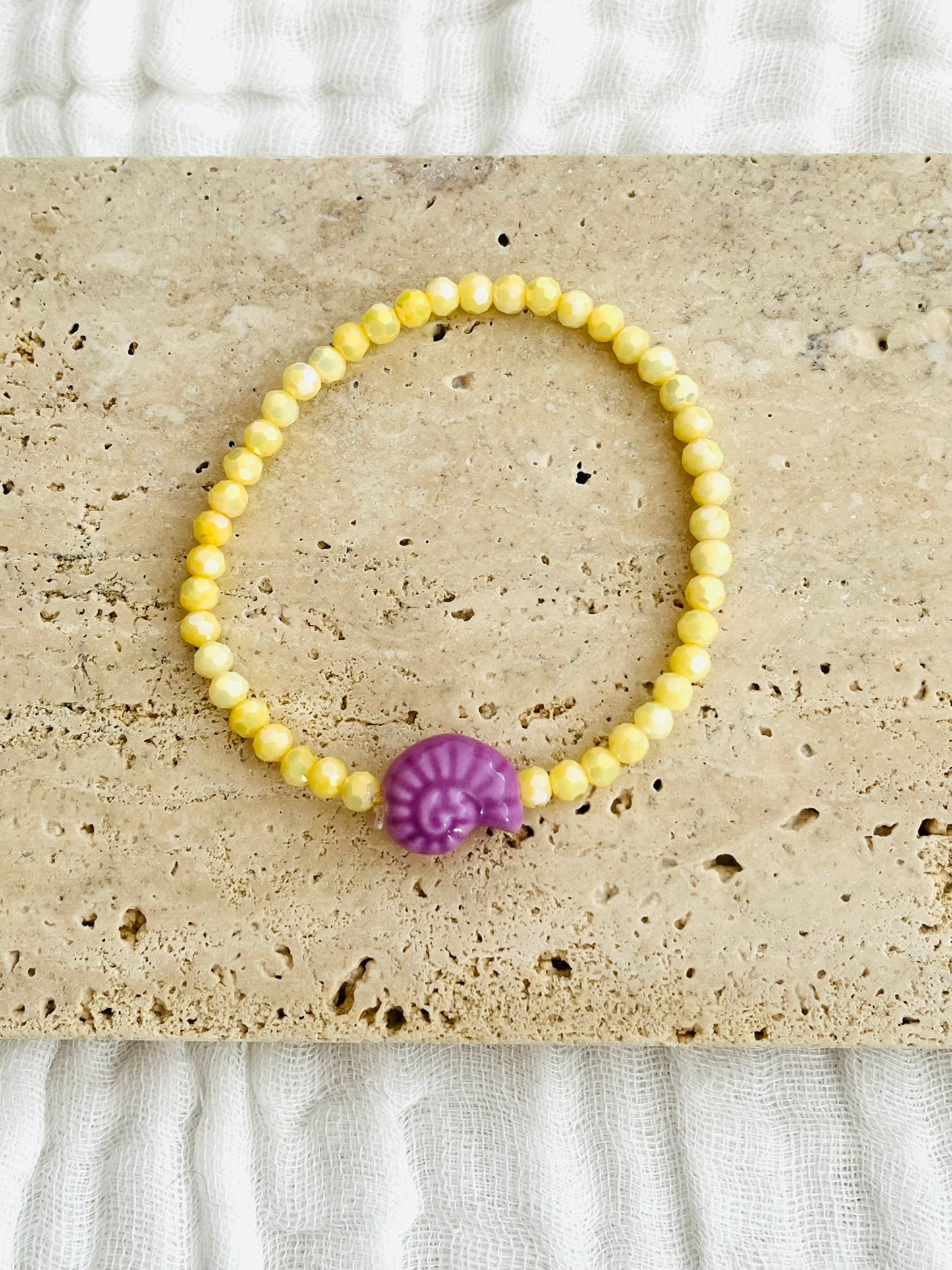 Bracelet élastique fait main.
Perles en verre facettées jaune et perle coquillage en céramique violet.
Bijou fait main.