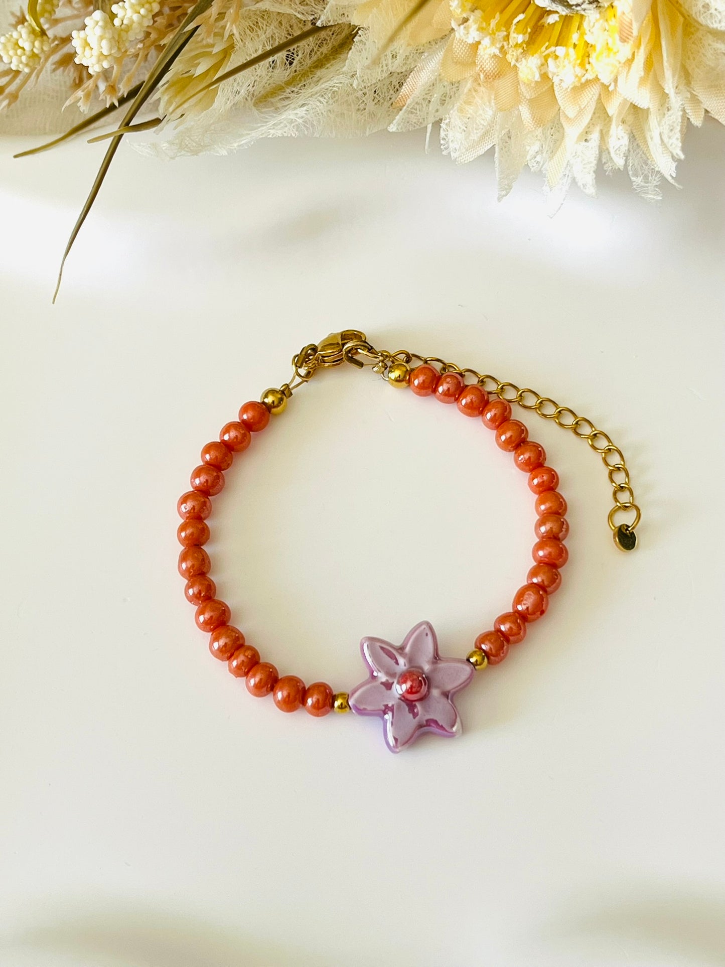 Bracelet fantaisie fait main.
Perles en verre orange nacré, perle fleur en céramique violet.
Fermoir en acier inox doré.
Bijou fait main.