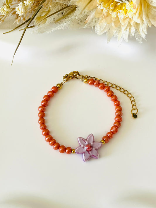 Bracelet fantaisie fait main.
Perles en verre orange nacré, perle fleur en céramique violet.
Fermoir en acier inox doré.
Bijou fait main.