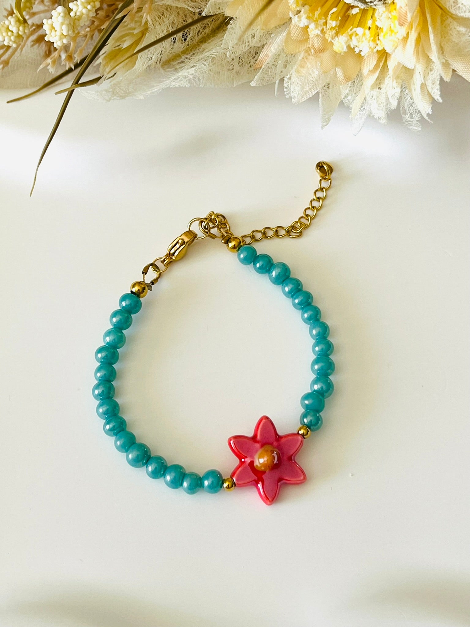 Bracelet fantaisie fait main.
Perles en verre turquoise nacré, perle fleur en céramique rouge.
Fermoir en acier inox doré.
Bijou fait main.