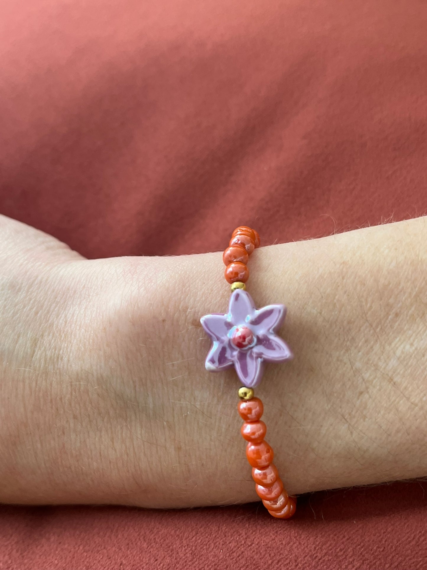 Bracelet fantaisie fait main.
Perles en verre orange nacré, perle fleur en céramique violet.
Fermoir en acier inox doré.
Bijou fait main.